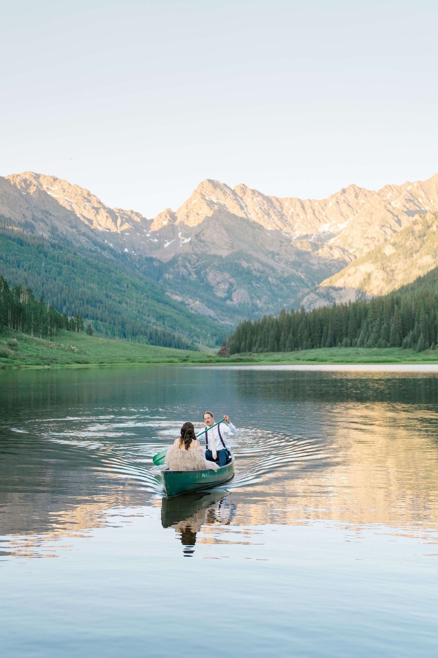 Piney River Ranch Wedding Couple in a canoe on a serene mountain lake at golden hour, surrounded by pine forests and rocky peaks.