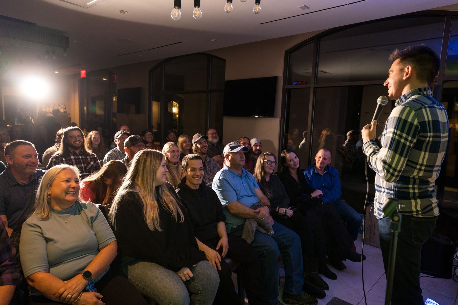 A crowded indoor venue with audience members watching a performer on stage under ambient lighting.