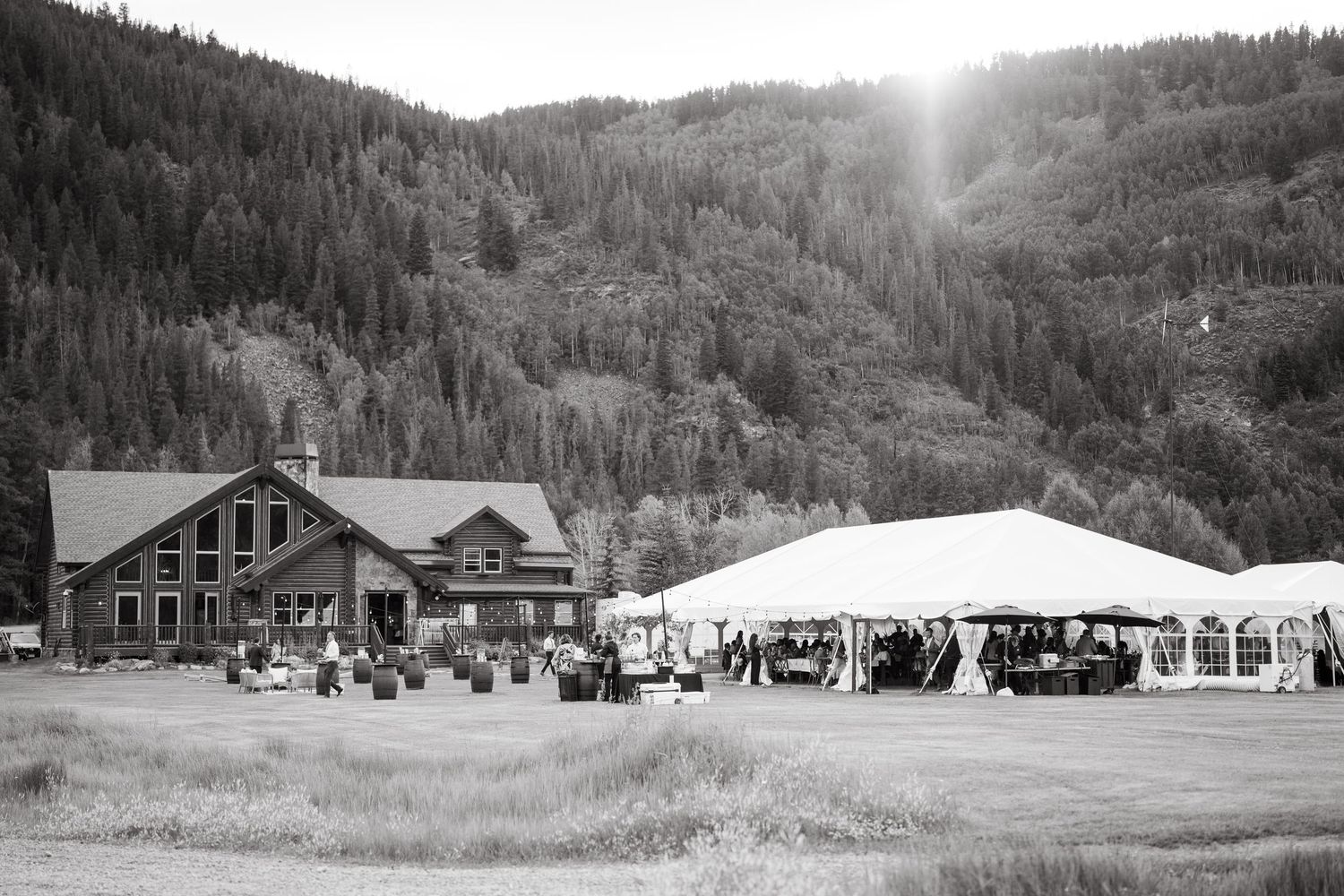 A panoramic black and white photo sequence showing a mountain lodge and gathering in a forested valley landscape.