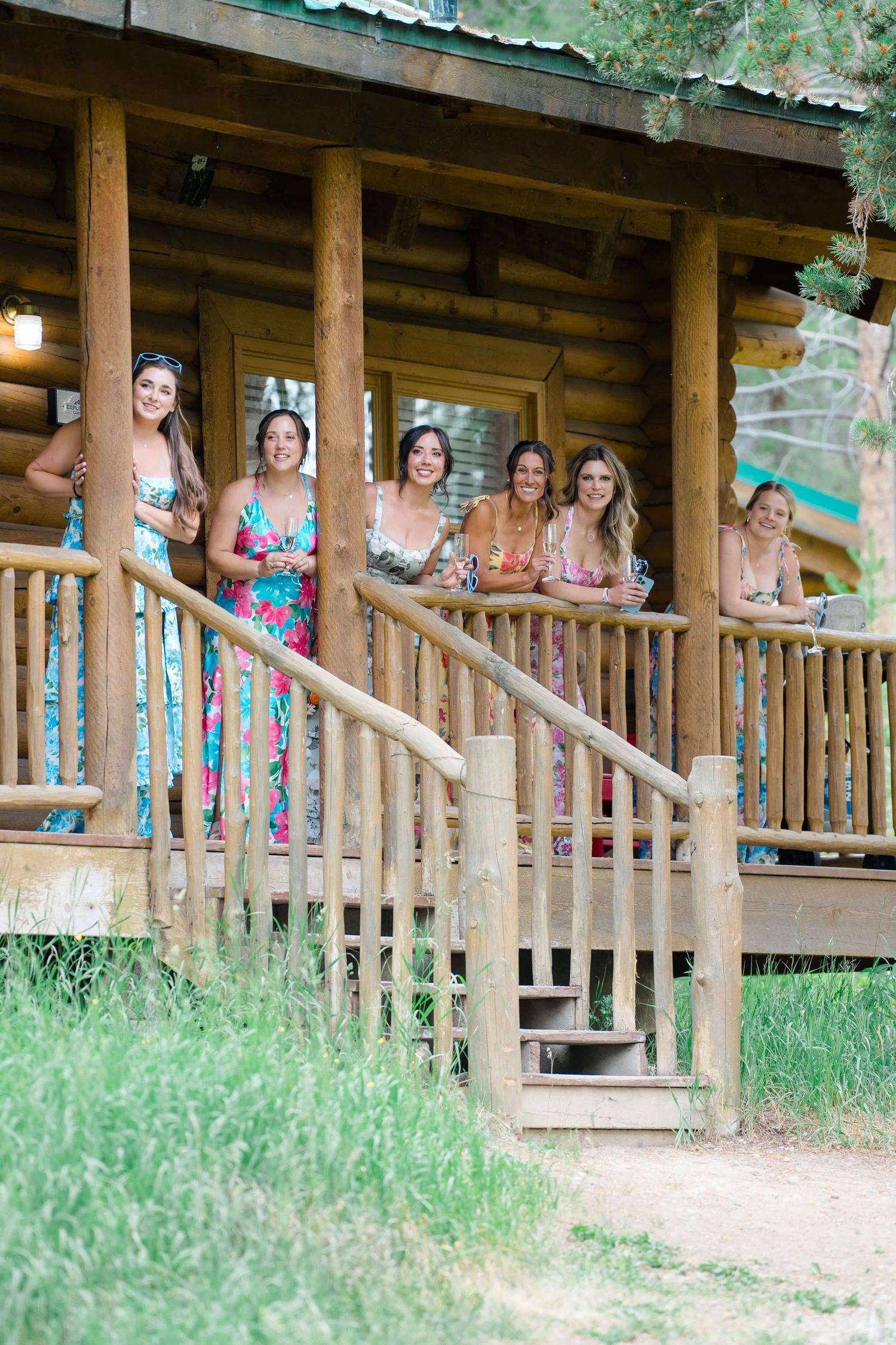 Camp Hale Wedding party in bright floral dresses gathered on rustic log cabin porch.