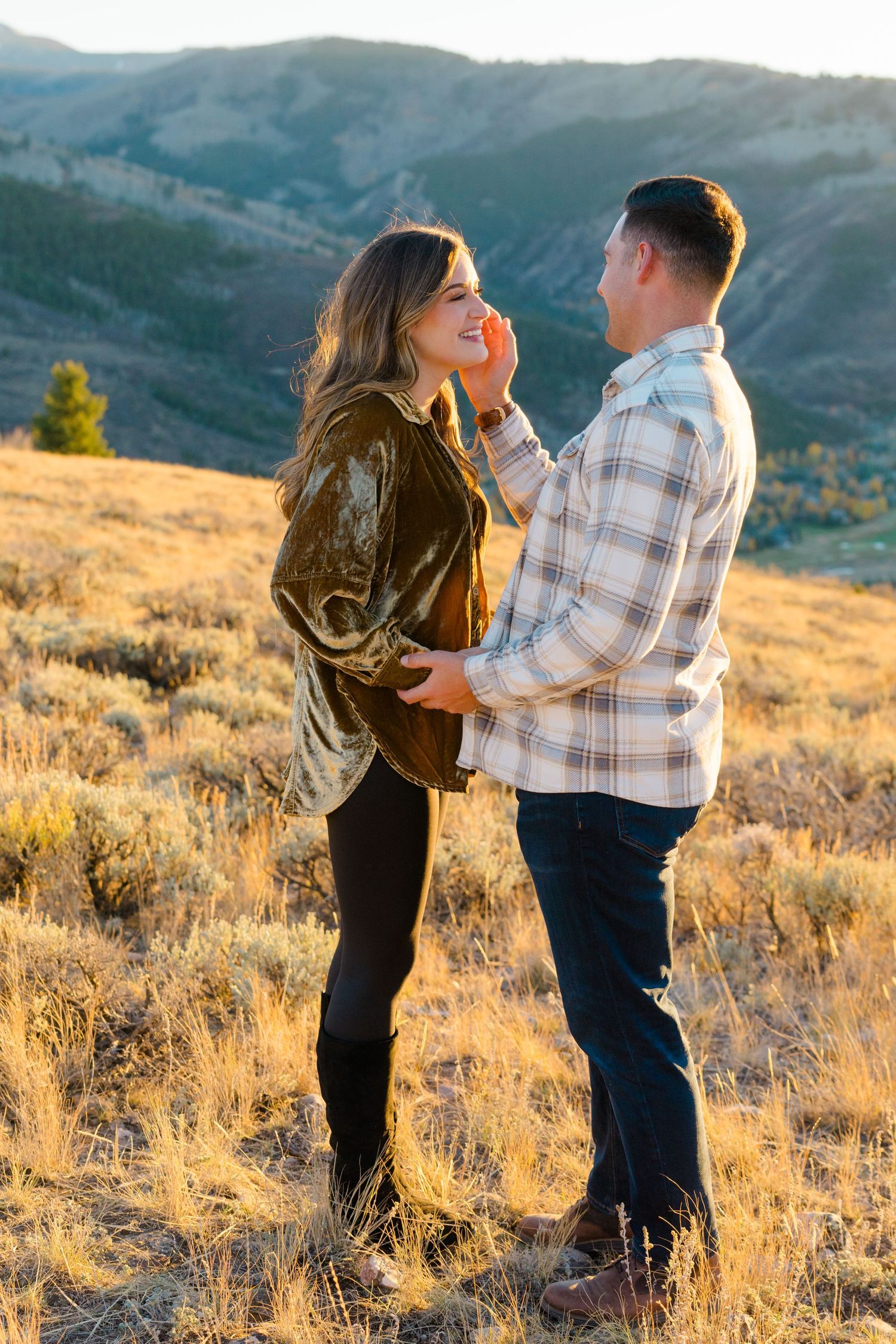 A couple shares tender moments in golden mountain meadow during sunset.