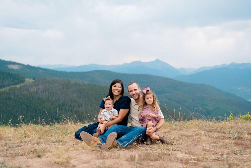 A scenic mountain landscape panorama showing a family relaxing together on a golden hillside with evergreen forests - best vail family photo