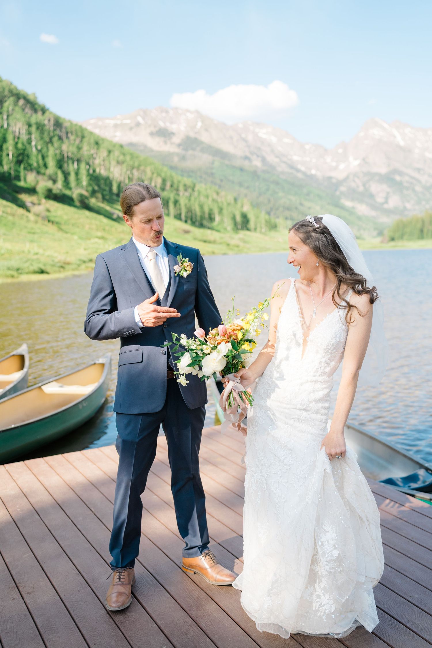 Wedding couple shares intimate moments on a lakeside dock with mountain views and canoes in the background.