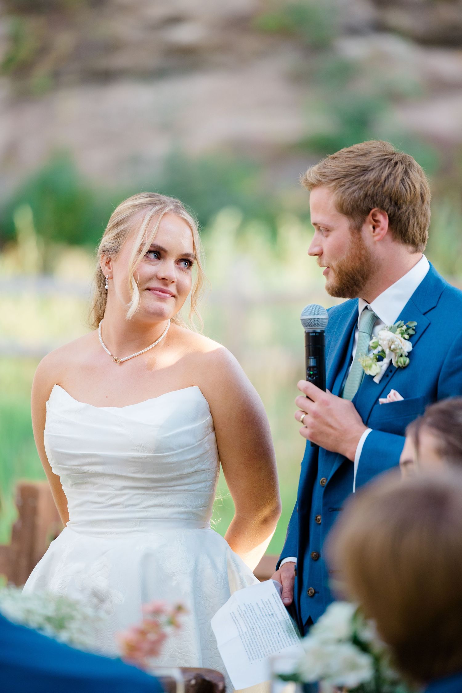Wedding ceremony moment with couple in blue suit and white dress exchanging vows outdoors.