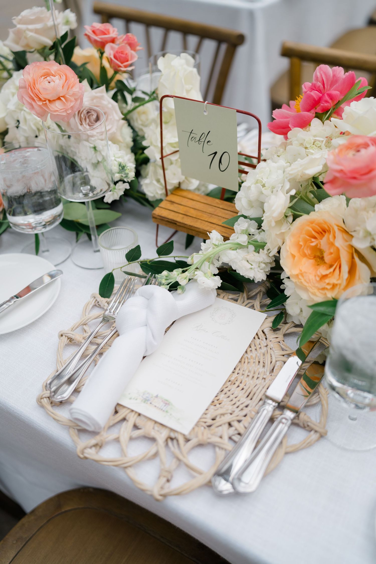 Elegant wedding table settings with coral and white floral centerpieces, woven placemats, and crystal glassware.