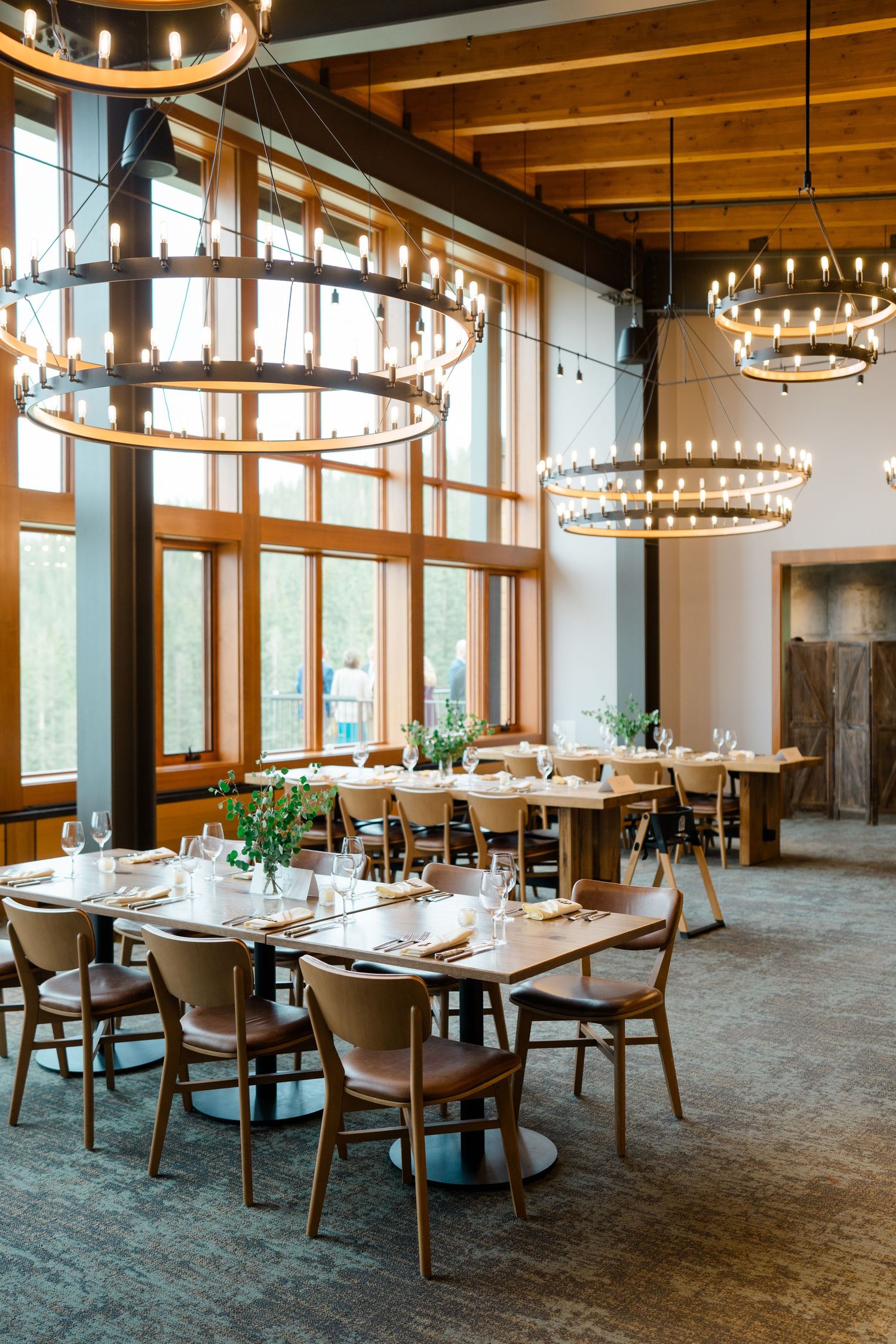 Elegant restaurant dining room with circular chandeliers, wooden tables, and teal carpeting in a modern rustic setting at copper mountain.