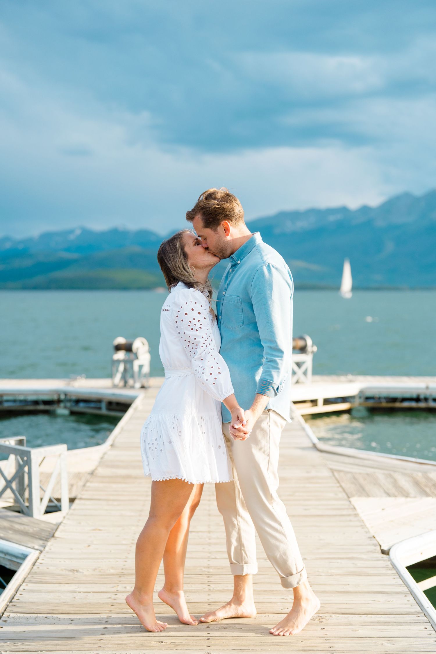 Lake Dillon Engagement - A romantic couple shares an intimate moment on a wooden dock overlooking a scenic mountain lake with sailboats.