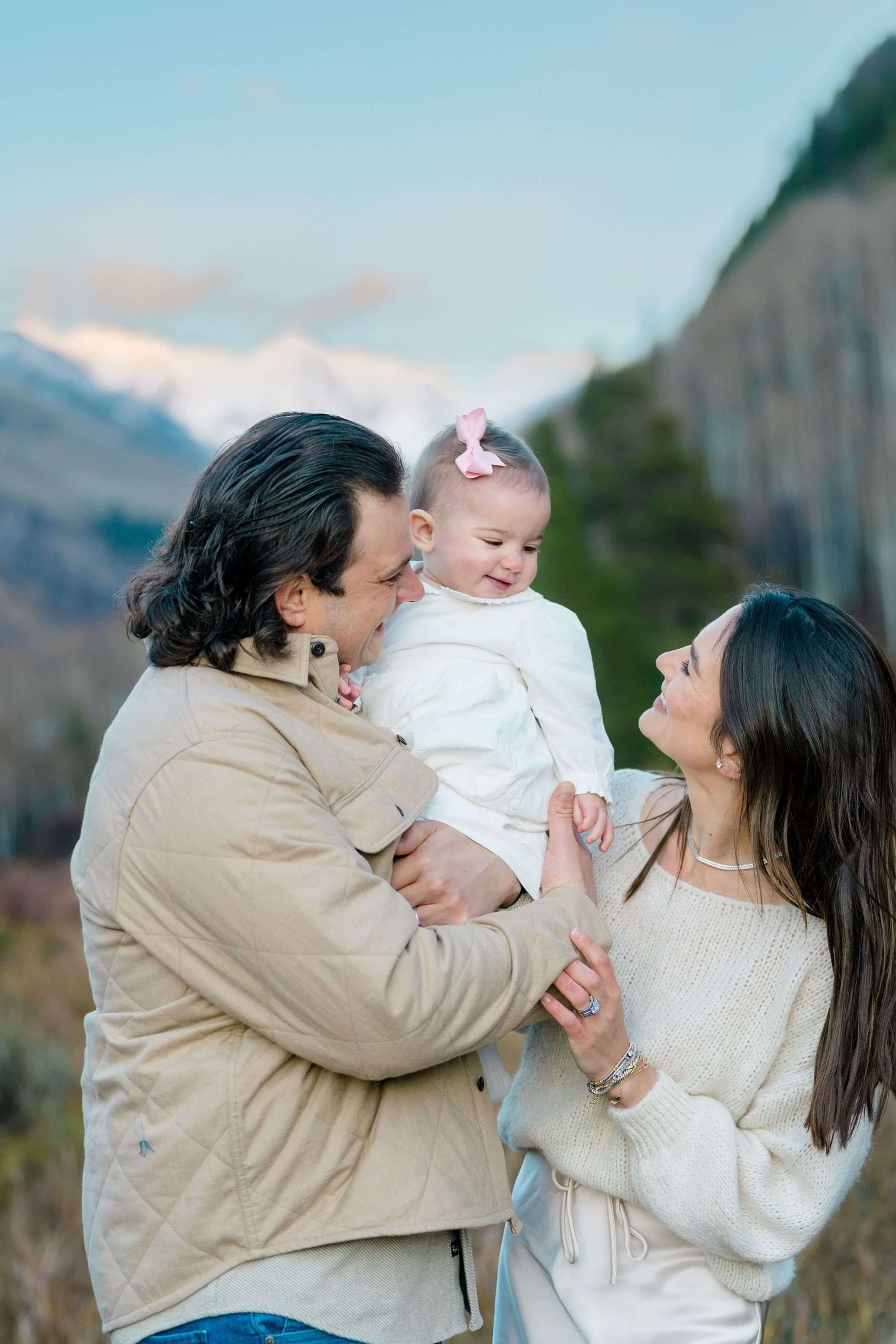 A loving family plays together outdoors against a scenic mountain backdrop during a sunset photoshoot.