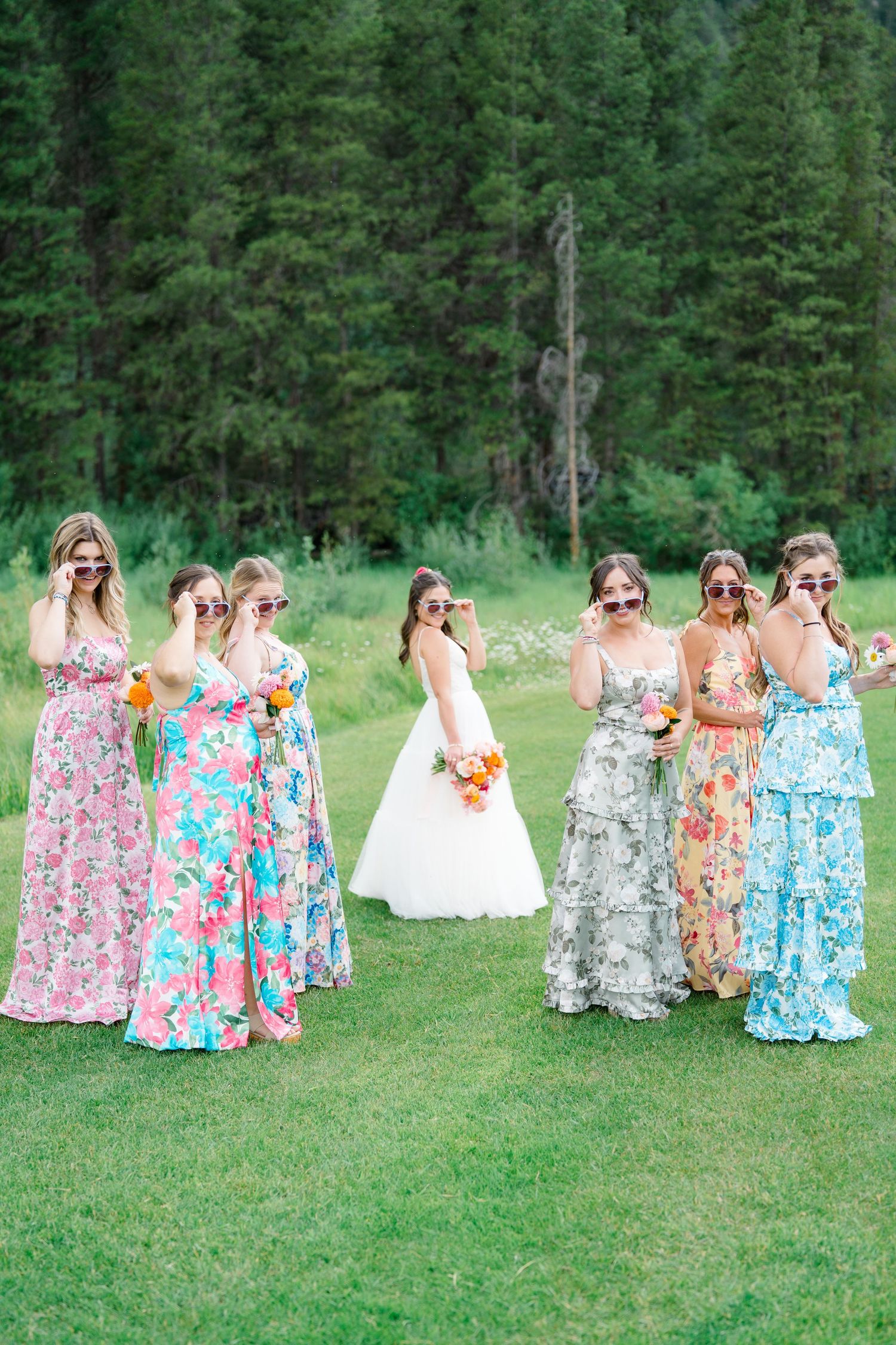 Candid moments of wedding party in colorful floral dresses enjoying themselves on a sunny meadow.