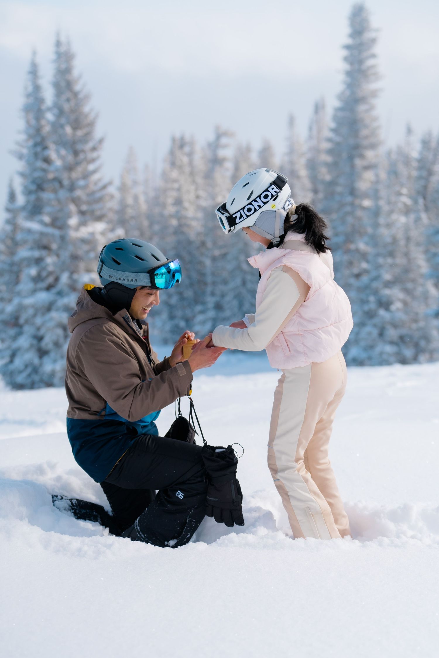 Two people play together in deep winter snow with snow-covered evergreen trees creating a magical backdrop.