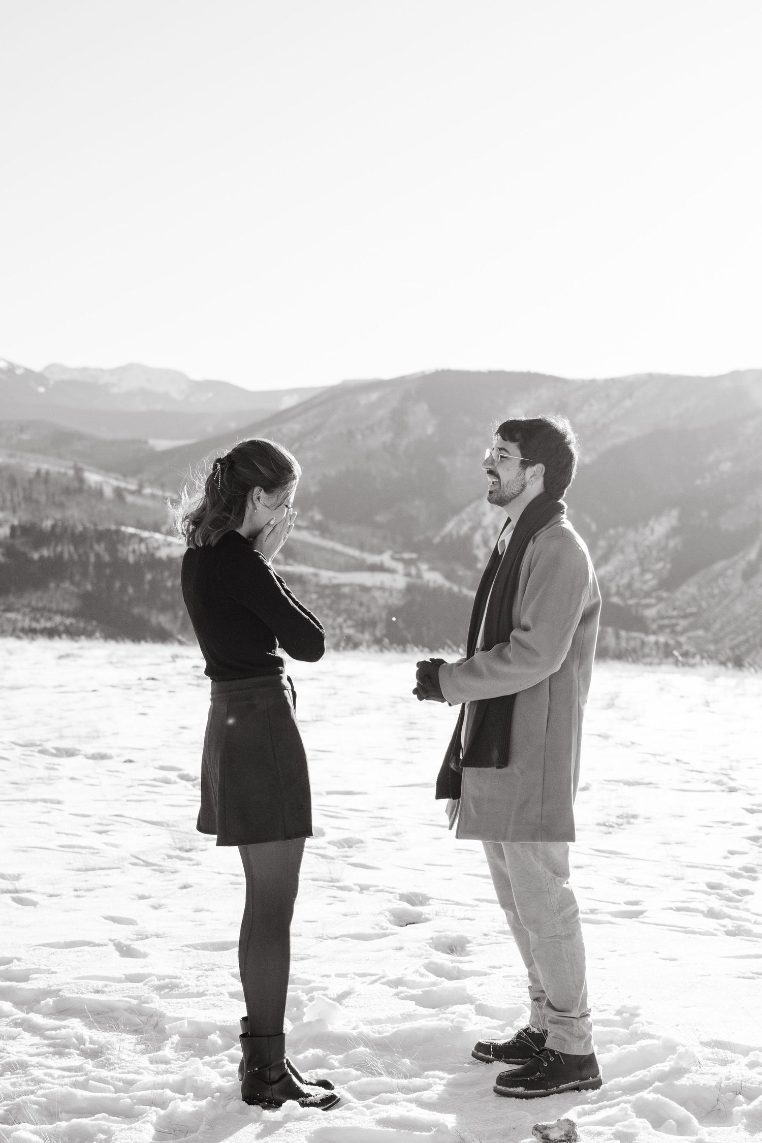 A sequence of black and white photos shows two people playfully interacting in a snowy winter landscape with mountains.