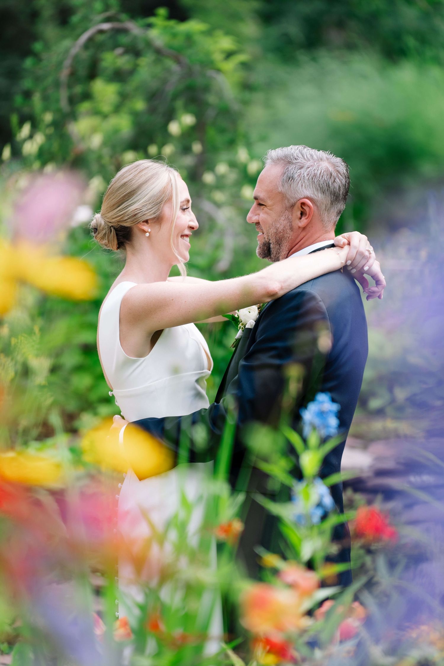Vail Wedding Venue - Smiling bride and groom embrace among colorful garden flowers, sharing a joyful moment in wedding attire.