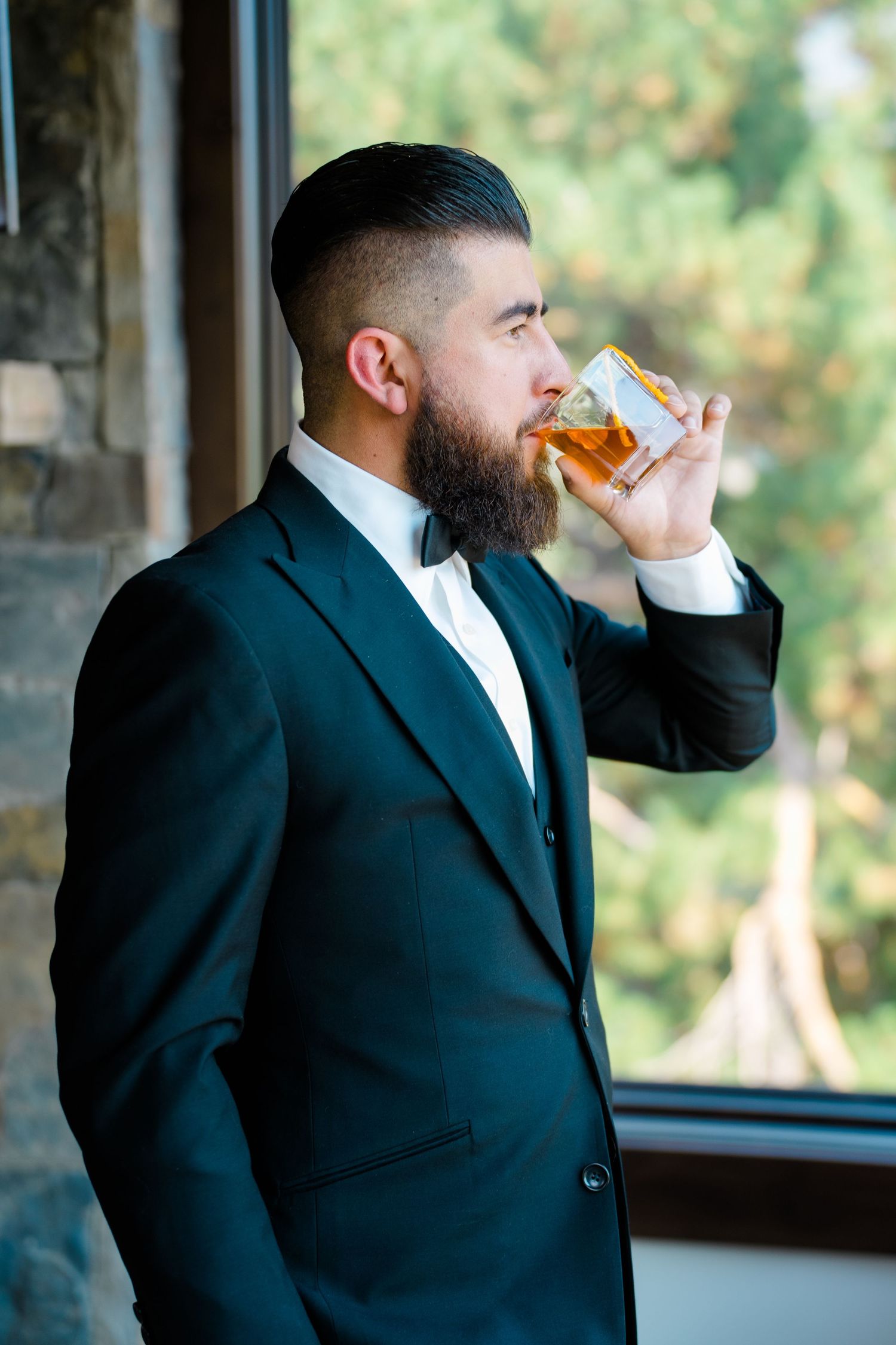 A person in a black suit drinks from a glass in a sequence of four similar photos by a window during Breckenridge wedding.
