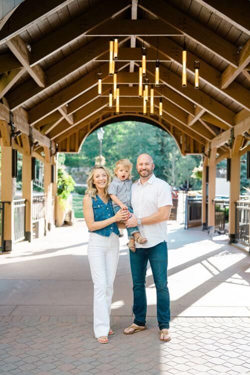 Family walking and playing together under a covered outdoor walkway with wooden beams and brick pavement - best vail family photo locations
