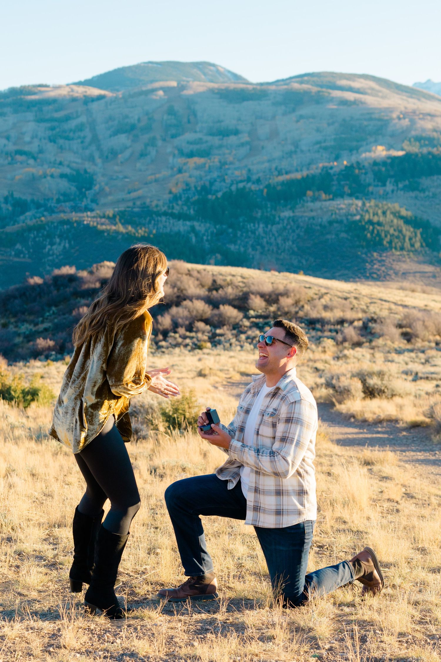 A couple gets engaged during a scenic golden hour photoshoot in the rolling hills of a mountain landscape.