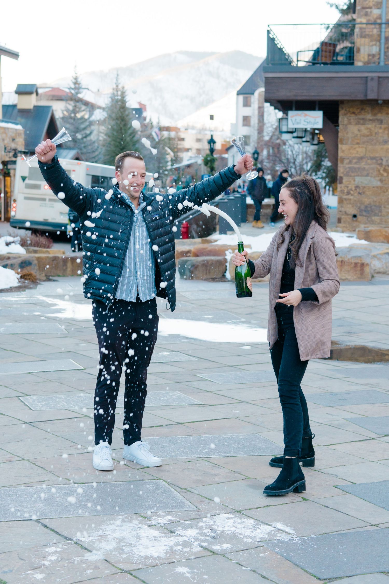 Two people playing and throwing snow at each other on a stone patio during winter.