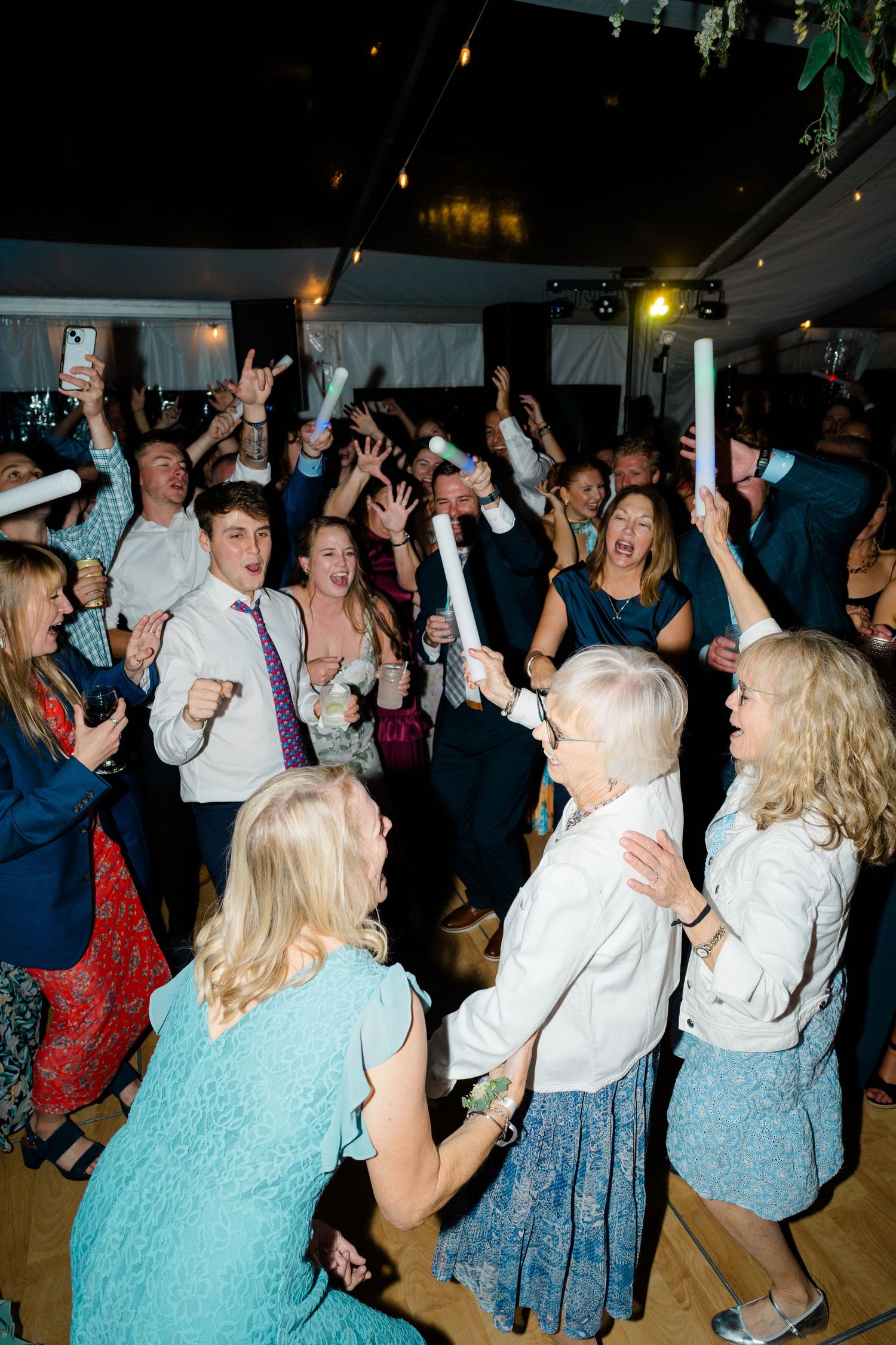 Wedding reception dance party with guests dancing and celebrating under evening tent lighting.