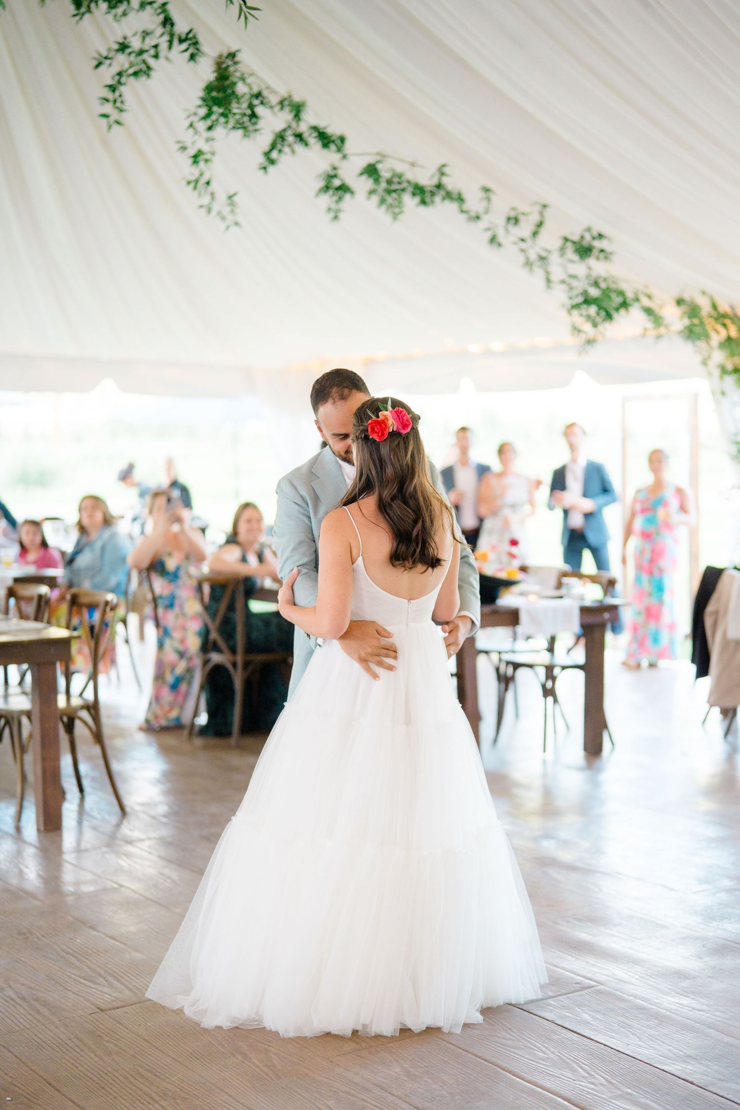 Wedding reception dance under a white tent decorated with greenery.