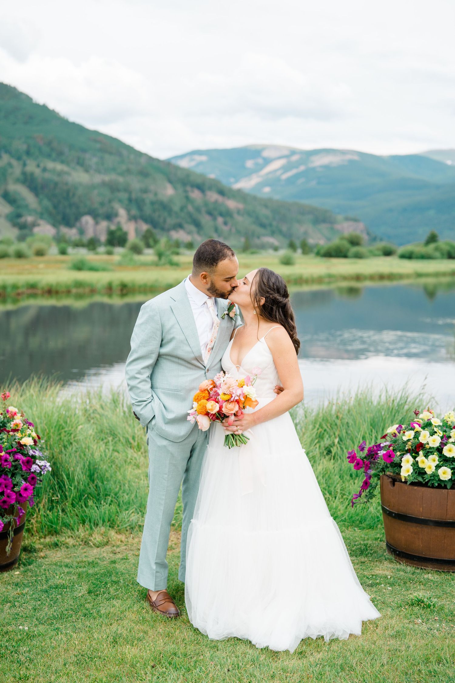 A romantic wedding photoshoot against a scenic mountain lake backdrop with vibrant floral bouquets.