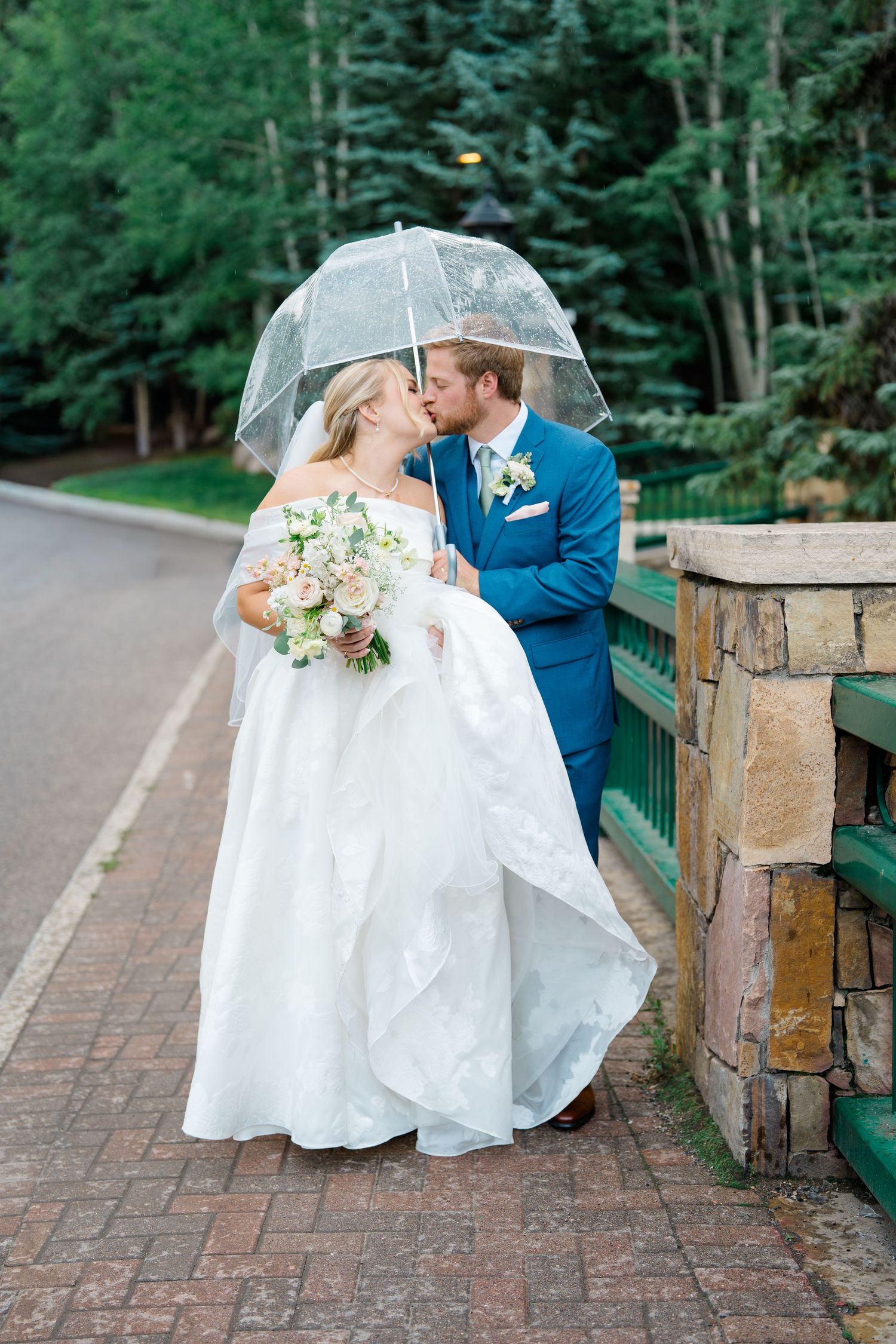 A romantic wedding couple shares intimate moments on a brick path surrounded by lush greenery.