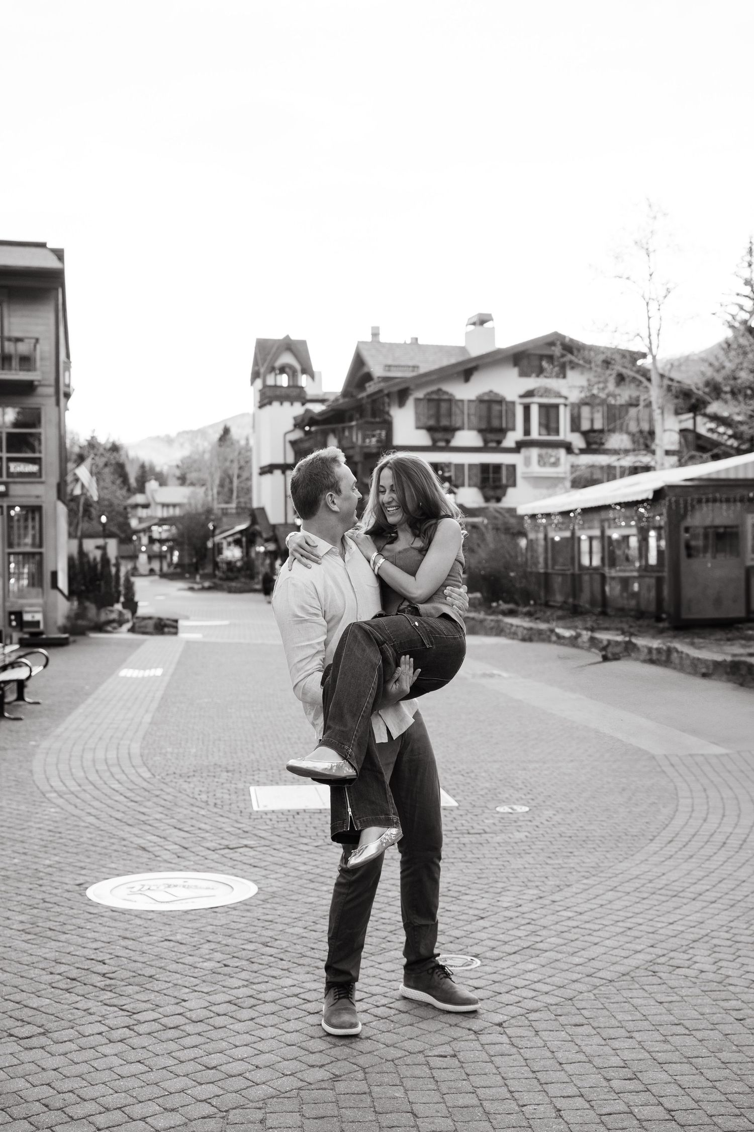 A couple embraces and kisses on a brick paved street in a black and white romantic moment.