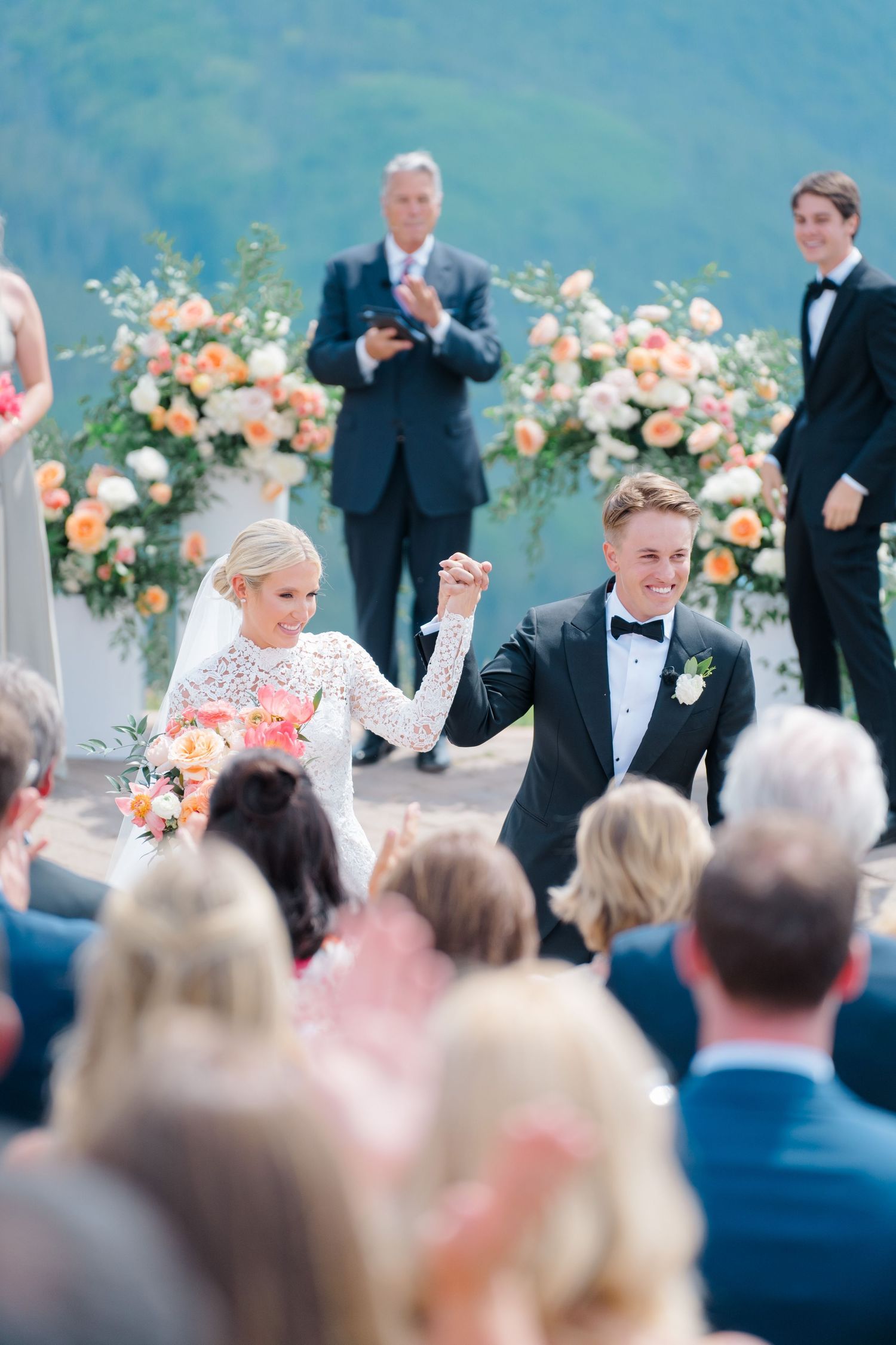 At Vail Wedding Deck Bride and groom raise joined hands joyfully at outdoor wedding ceremony with mountain backdrop.