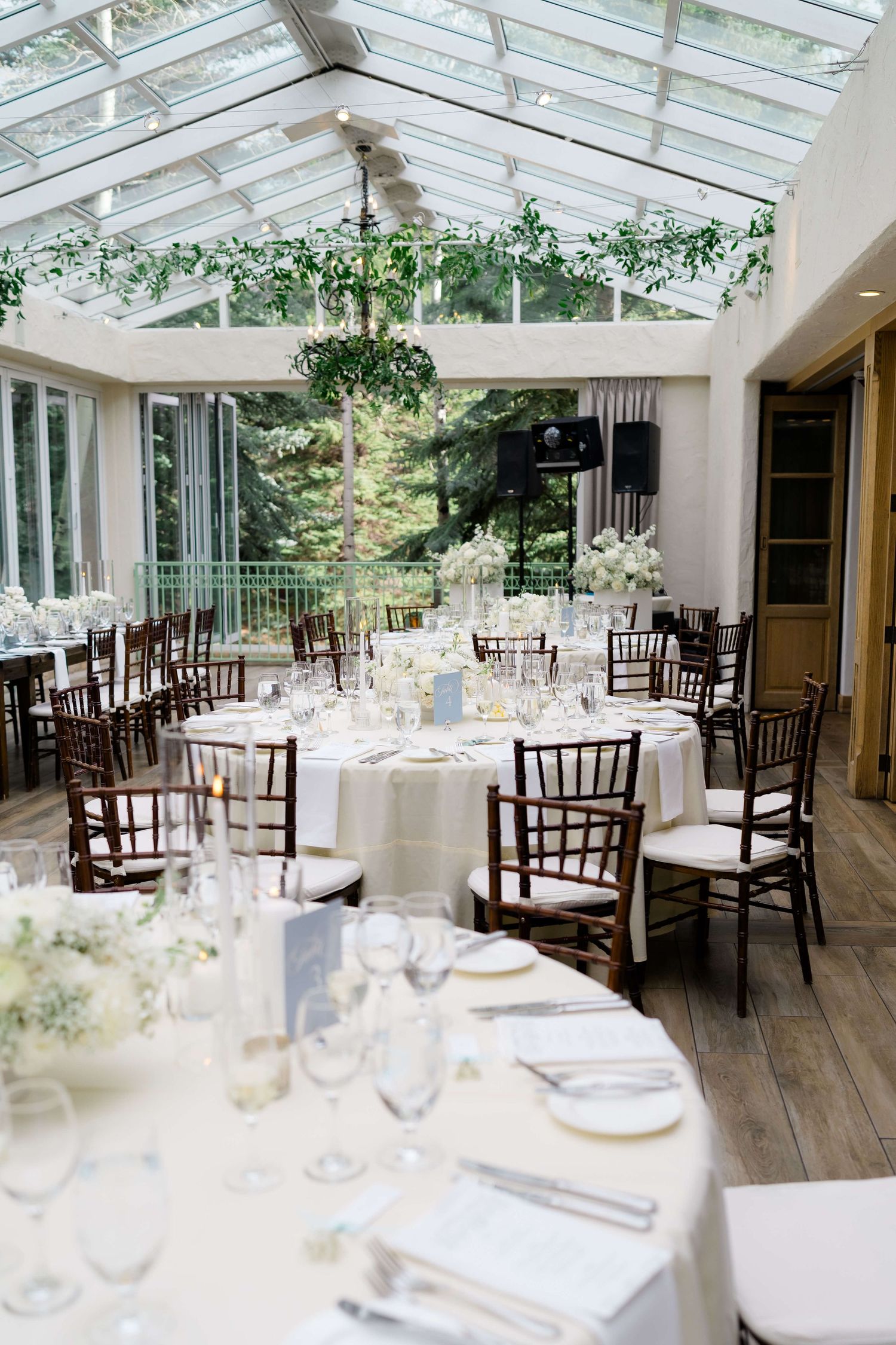 Elegant greenhouse wedding reception with white floral centerpieces, chiavari chairs, and glass ceiling venue at Vail Sonnenalp Wedding.