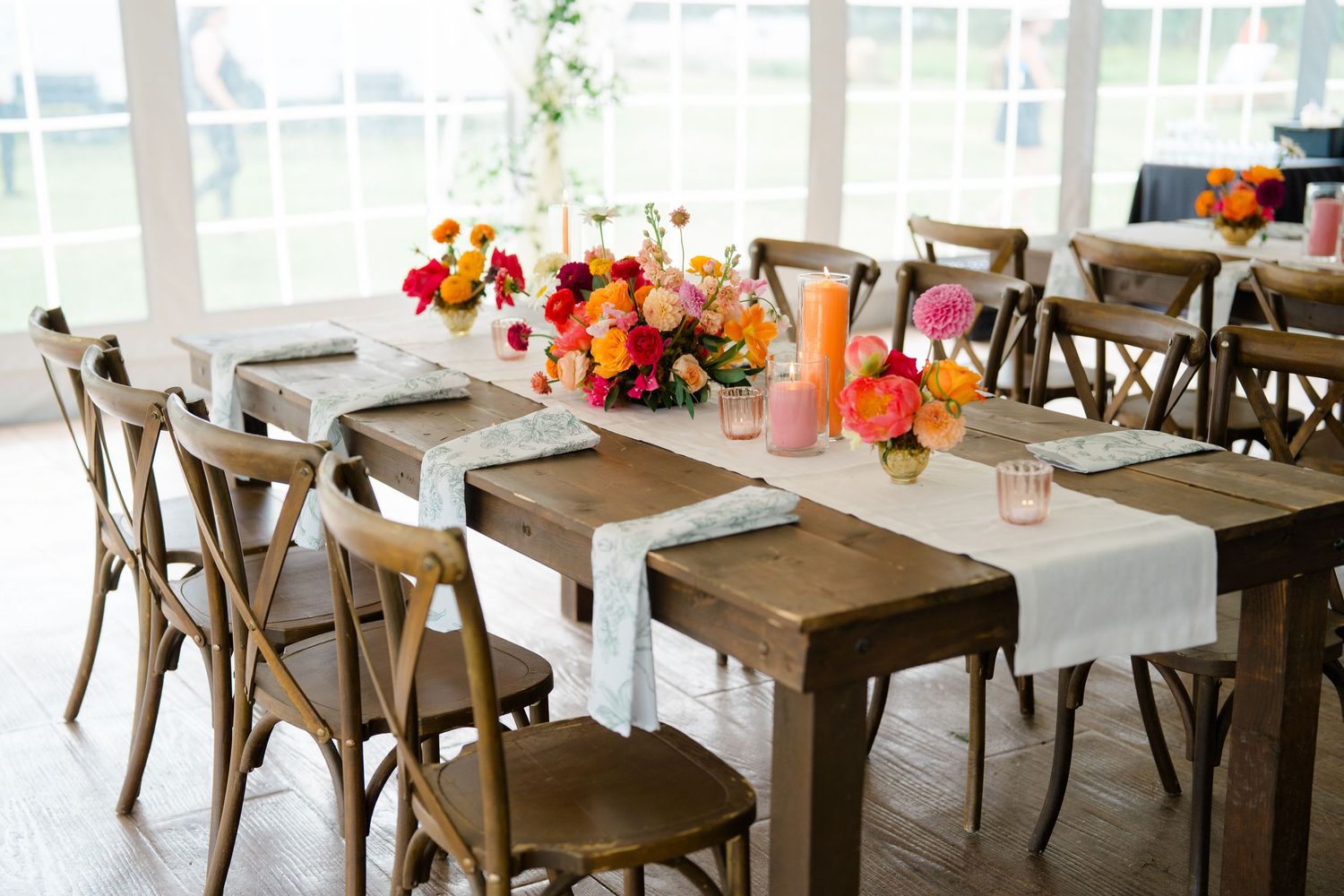 Rustic wooden dining tables with white chairs and colorful floral centerpieces in a bright restaurant setting.