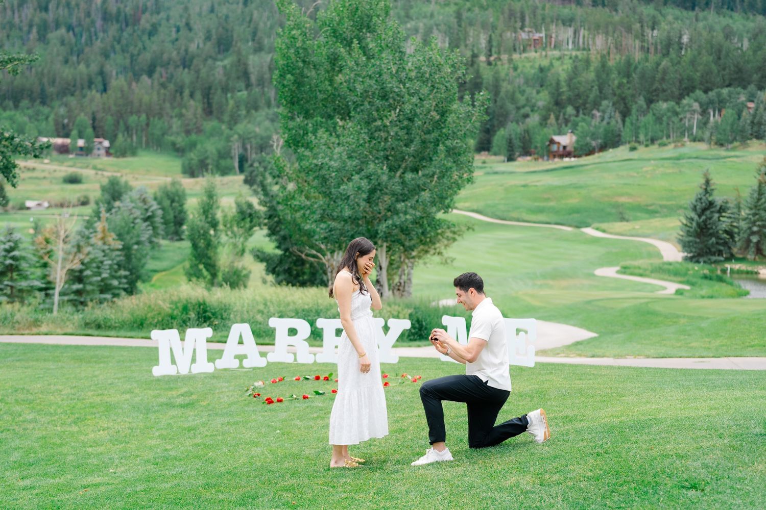 A couple shares a romantic moment on a lush green golf course with mountains in the background.