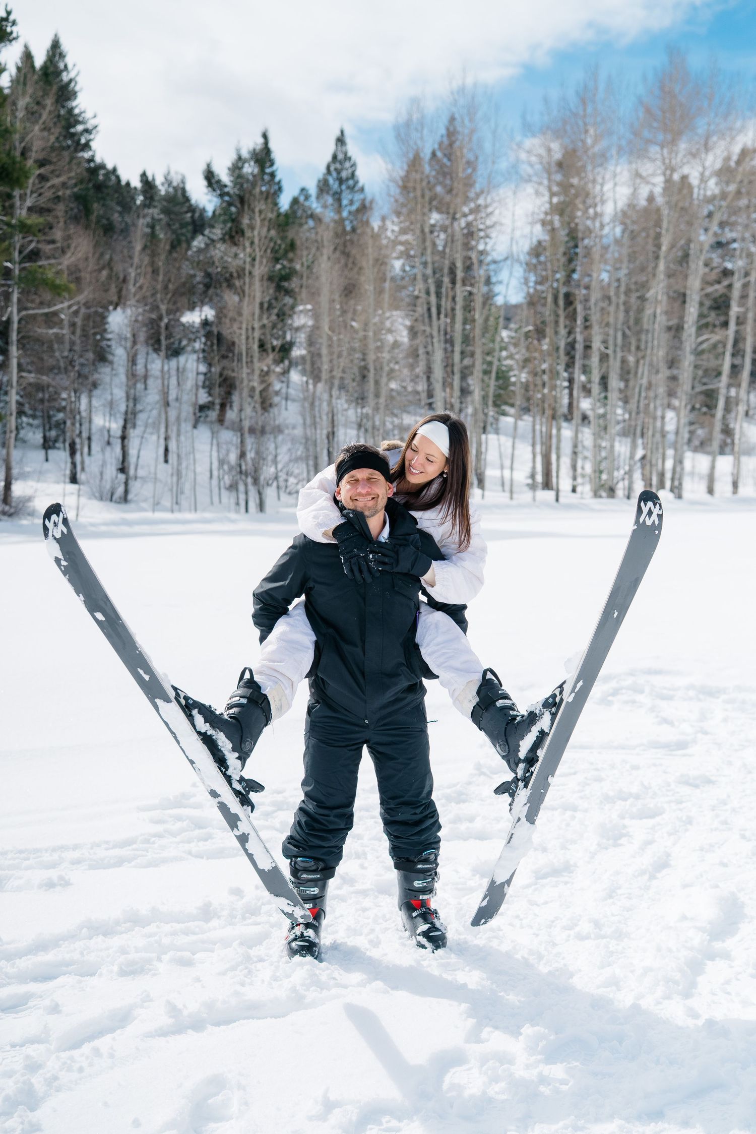 Two skiers enjoying a playful moment on snowy slopes with snow-covered trees in the background on a winter day.