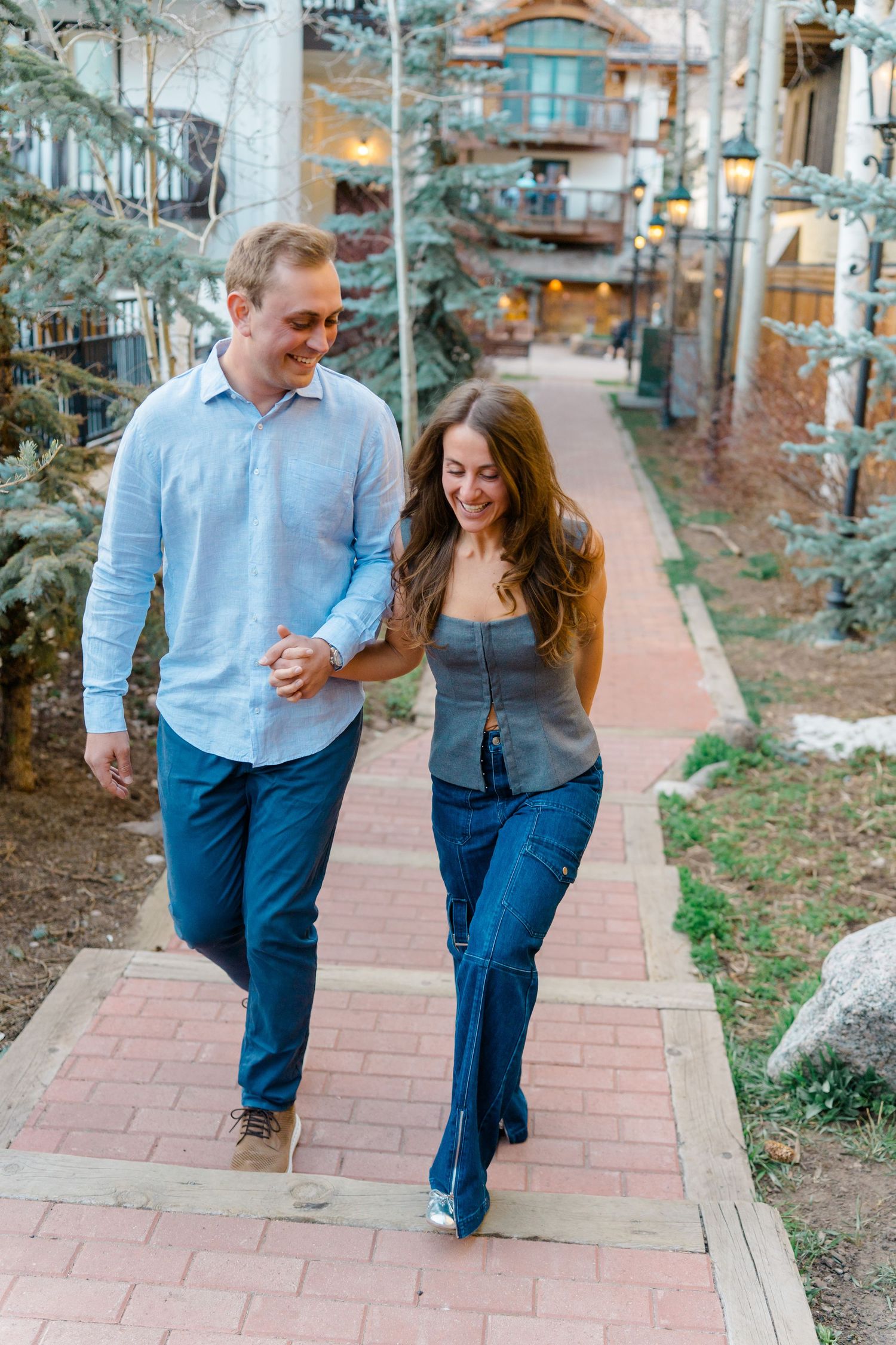 A couple walks together on a brick path while sharing a joyful moment in a mountain setting.