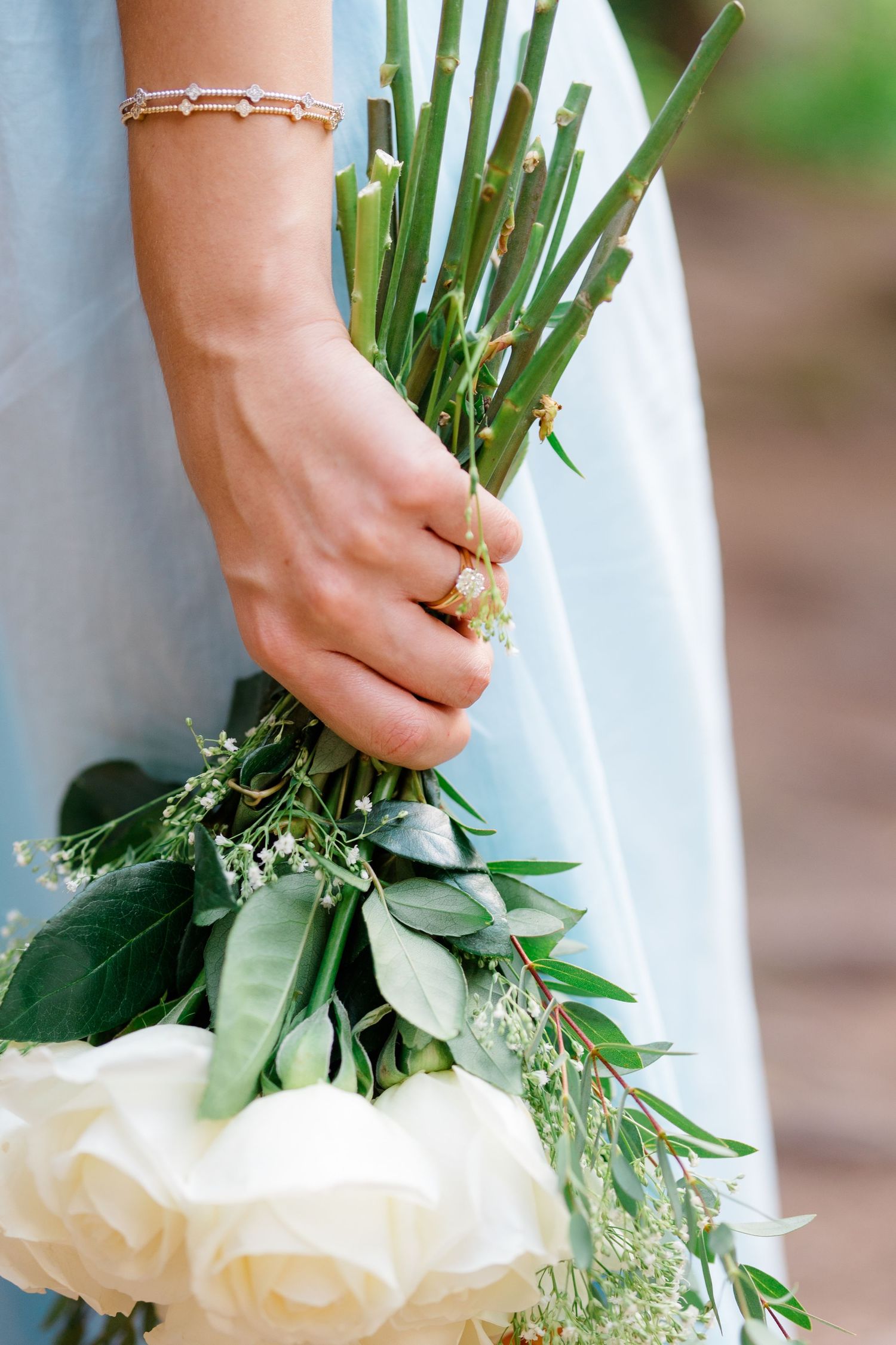 Close-up view of hands holding a delicate white rose and greenery bouquet against a blurred natural background.