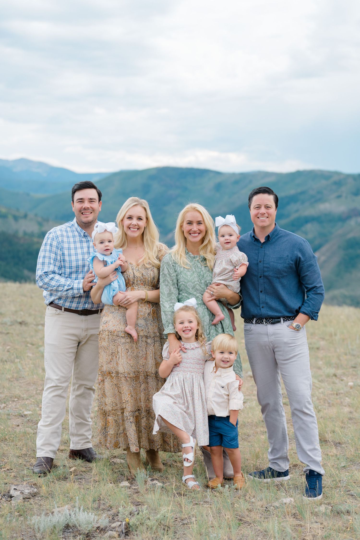 A group portrait of families standing together in casual attire against a mountain landscape backdrop.