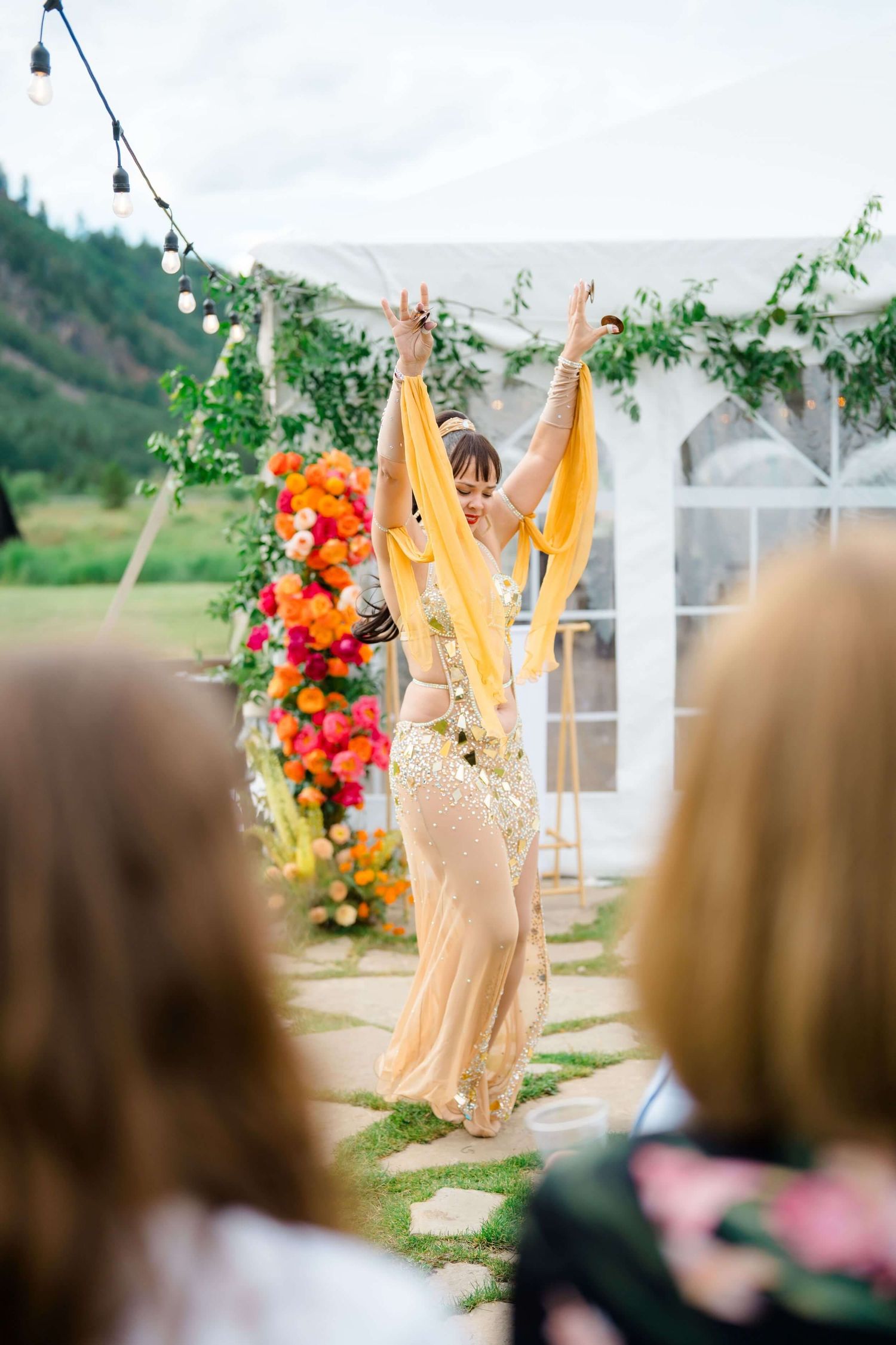A performer in gold dress dances at an outdoor camp hale wedding celebration with colorful floral arrangements.