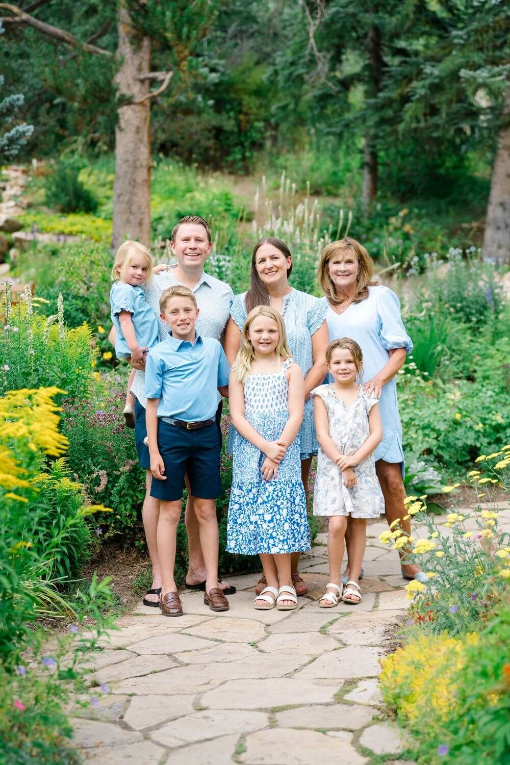 A group stands together on a stone path in a lush summer garden filled with yellow flowers and greenery - best vail family photo locations