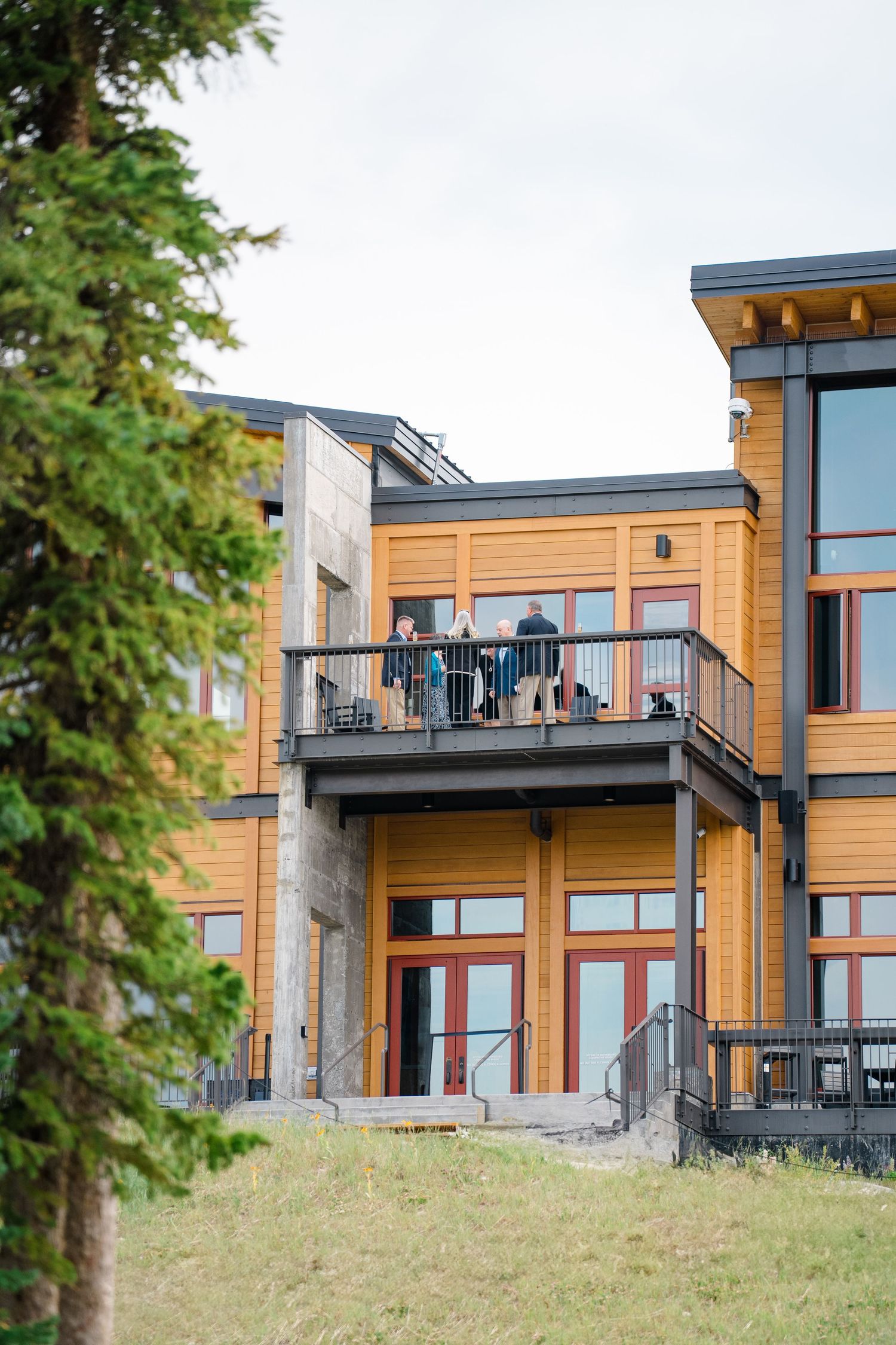 Modern wood-sided building with people gathered on an elevated balcony deck overlooking a grassy hillside at copper mountain.