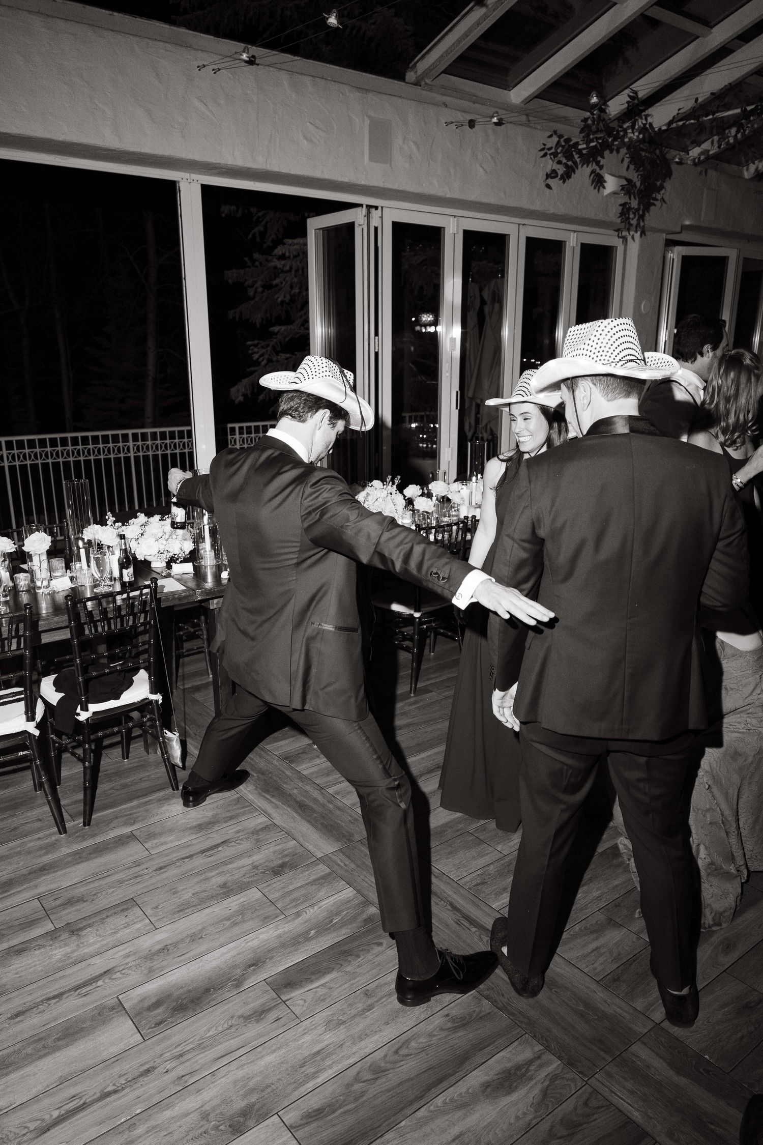 Men in cowboy hats dancing energetically at a formal event in black and white photo.