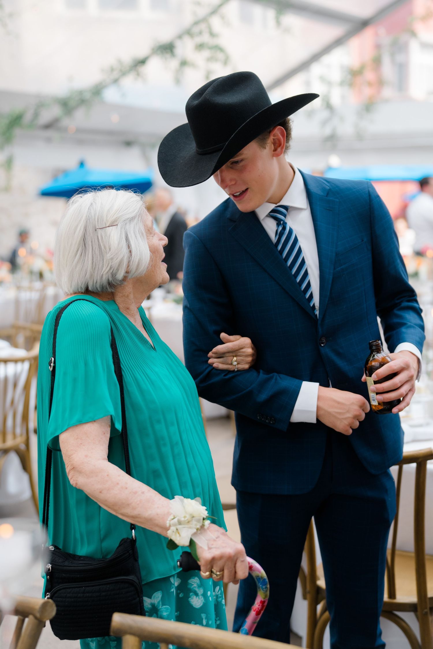 Elderly woman in teal dress chats with young man in navy suit and black cowboy hat at elegant wedding at  Arrabelle in Vail, Colorado.