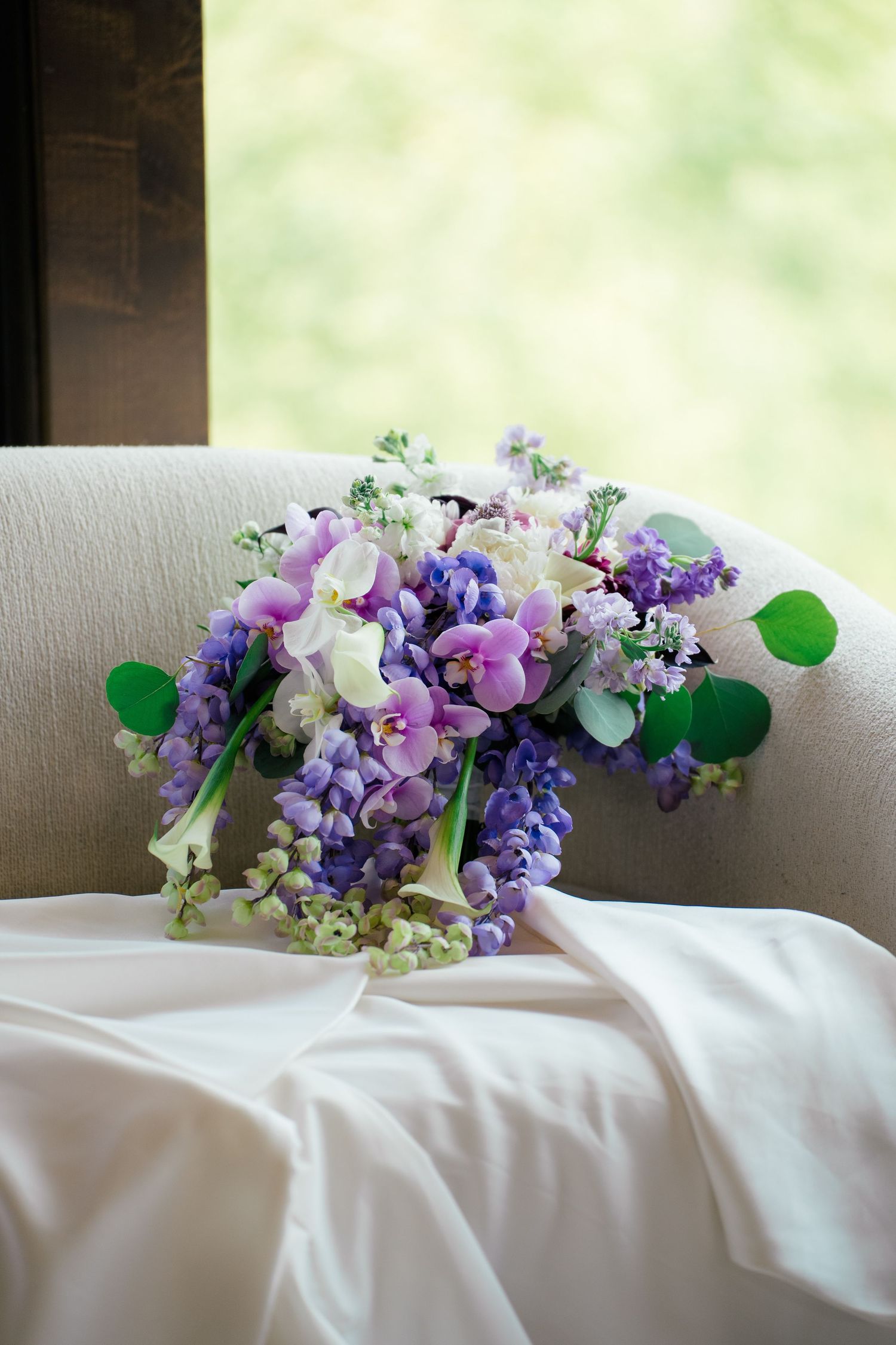 Purple and white floral arrangements with greenery displayed on white linens.