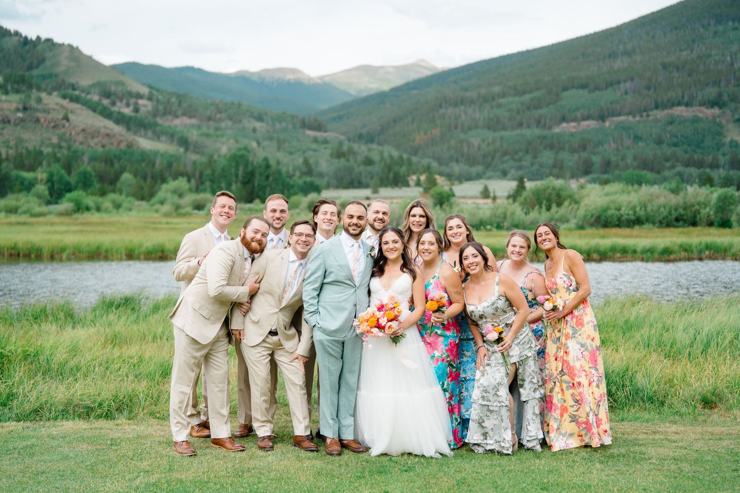 Wedding party poses in front of scenic mountain landscape during outdoor summer celebration.