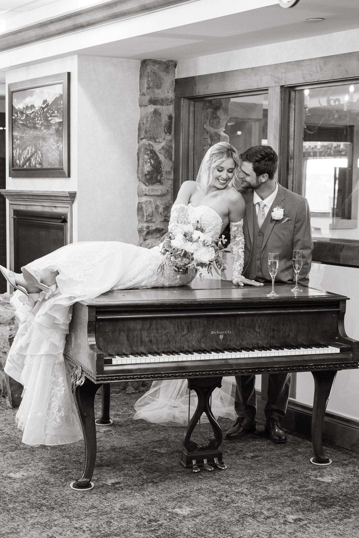 bride laying on piano with groom in ballroom
