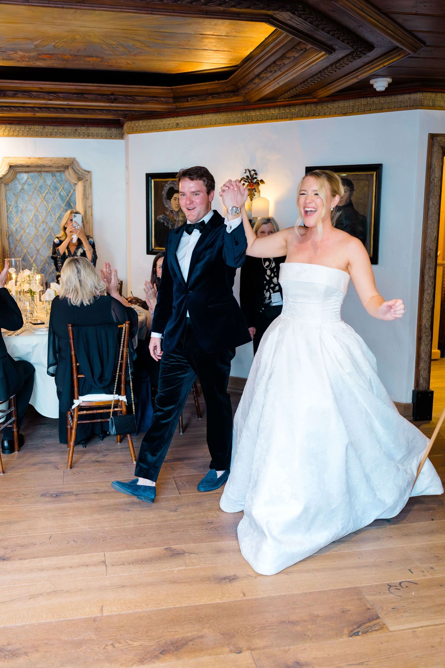 Bride and groom make joyful grand entrance at elegant wedding reception, she in strapless gown, he in black tuxedo.