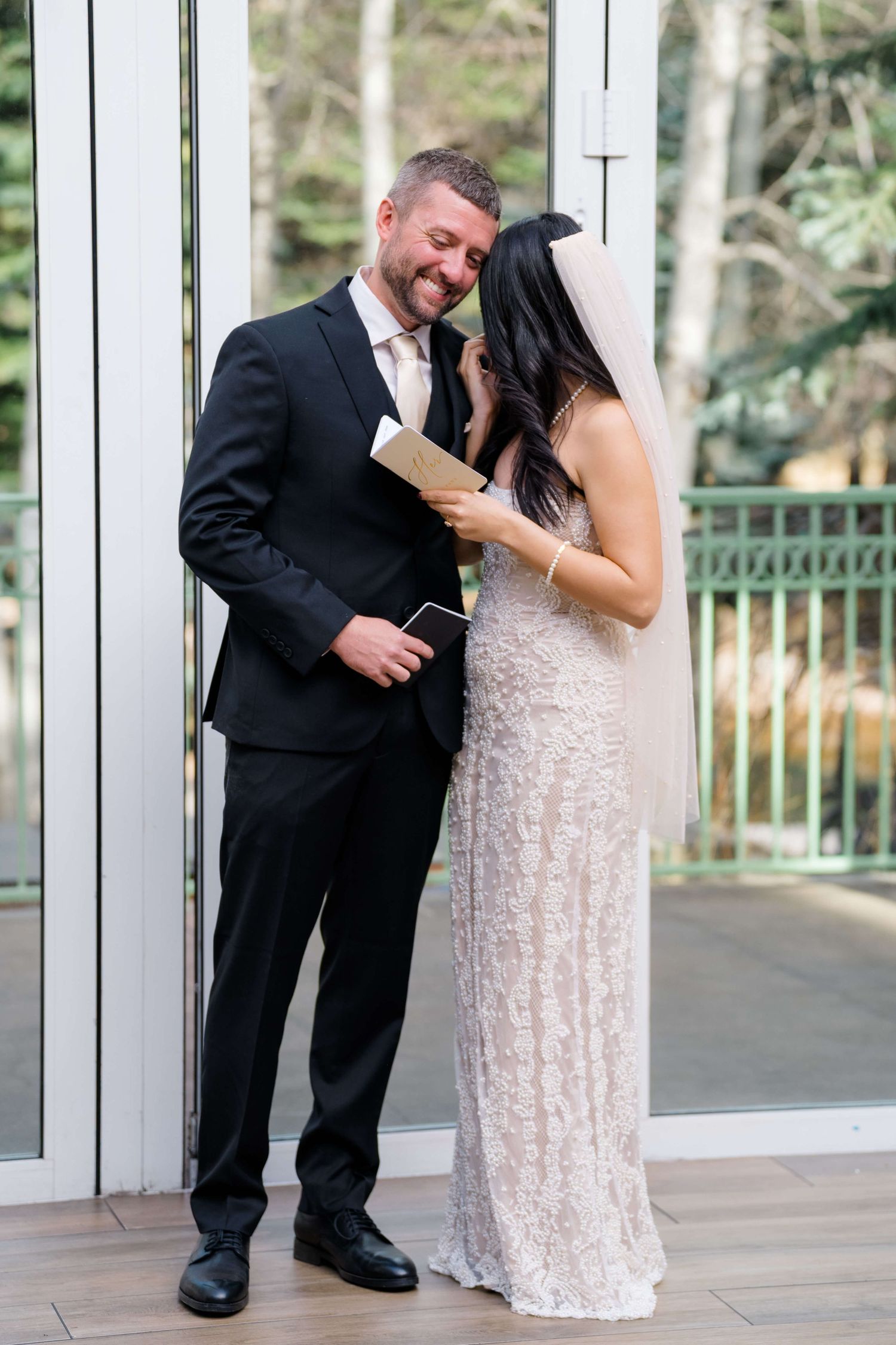 Bride and groom sharing an intimate moment reading vows together at indoor wedding ceremony.