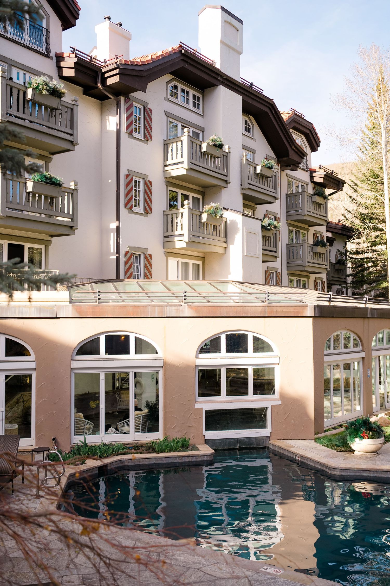 Luxury alpine hotel with balconies and flower boxes overlooks an elegant outdoor pool and glass-enclosed spa area at Vail Sonnenalp Wedding.