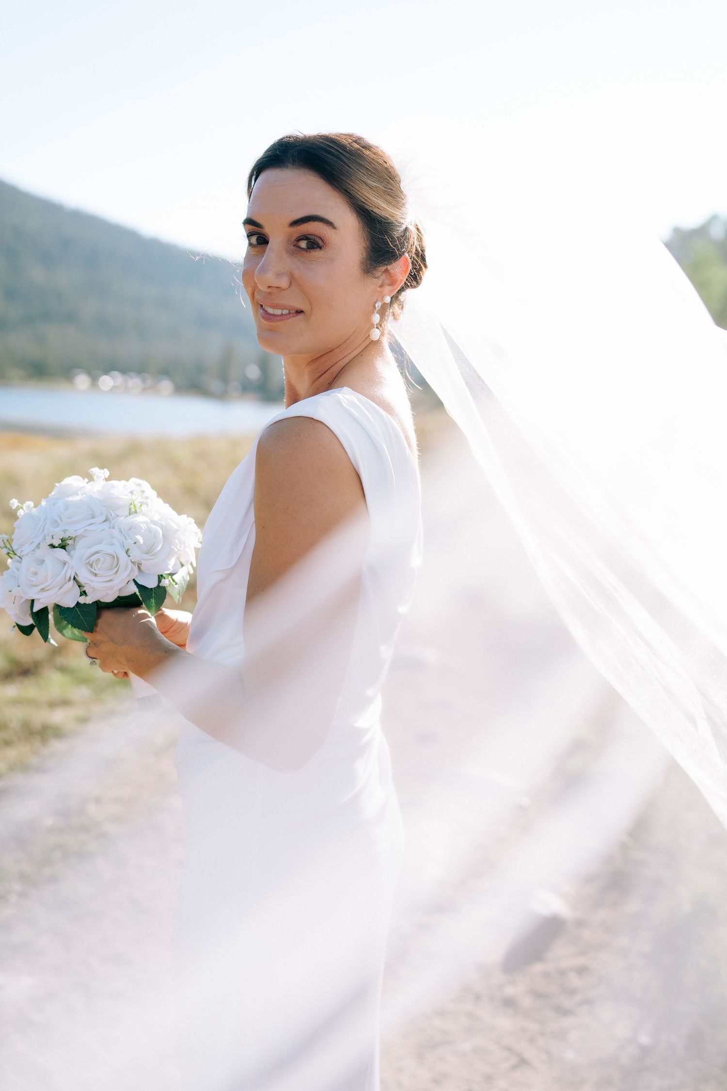 A bride in a white wedding dress holds a bouquet of white flowers against a scenic outdoor backdrop during piney river ranch elopement.