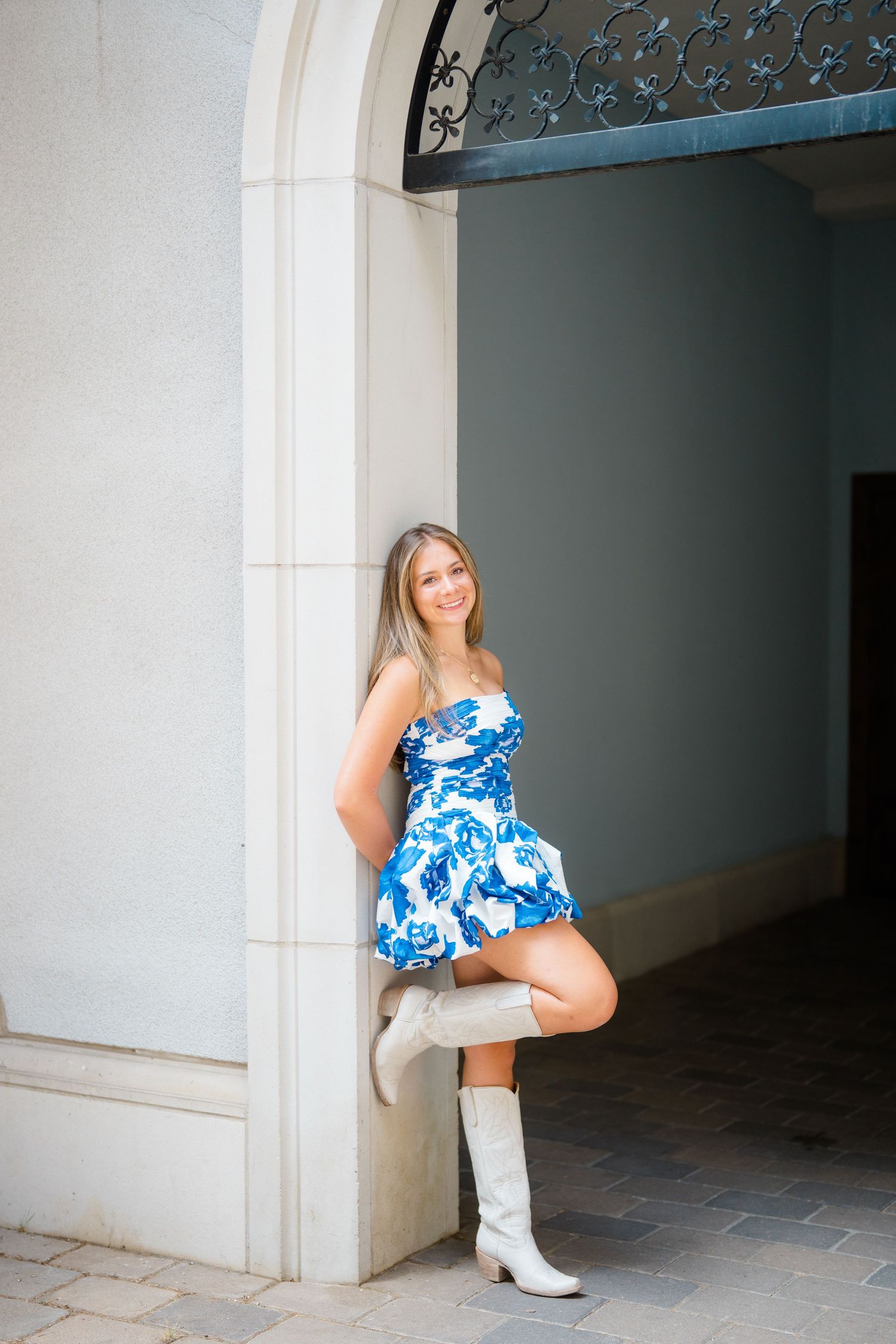 A blue and white floral dress paired with white boots creates a striking pose under an archway during vail senior photography session.