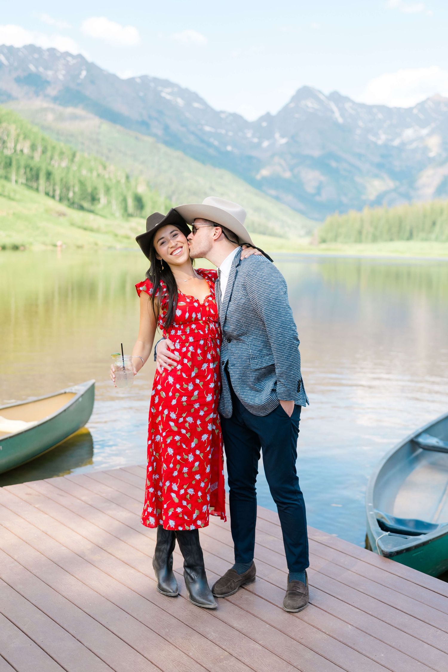 Couple posing on a lakeside dock at Piney River Ranch Wedding with mountain views, woman in red floral dress and man in gray.