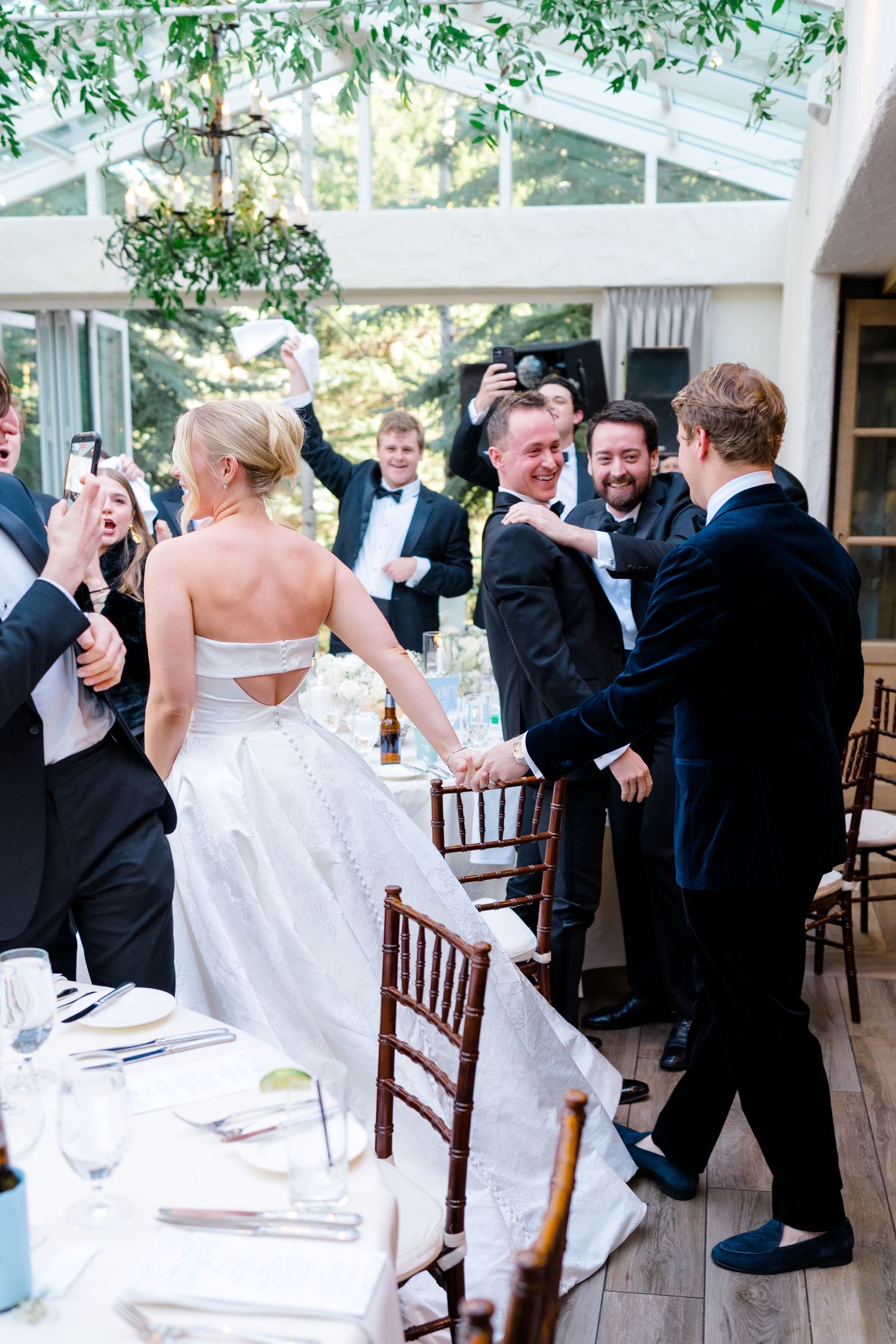 Vail Wedding Photographer captures bride in gown greets smiling guests in tuxedos at elegant wedding reception in glass conservatory.