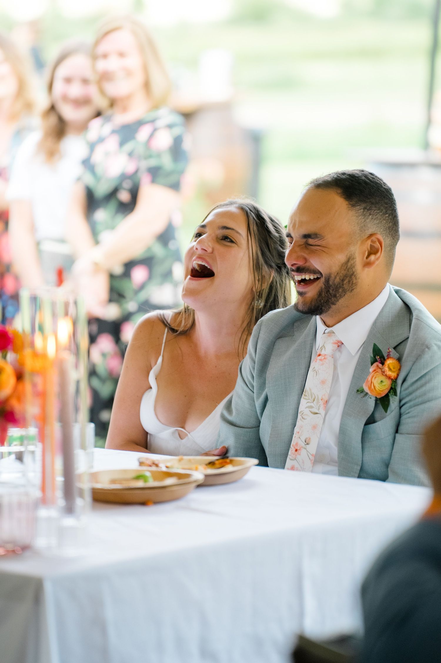 Wedding couple sharing a joyful laugh during reception speeches at their table.