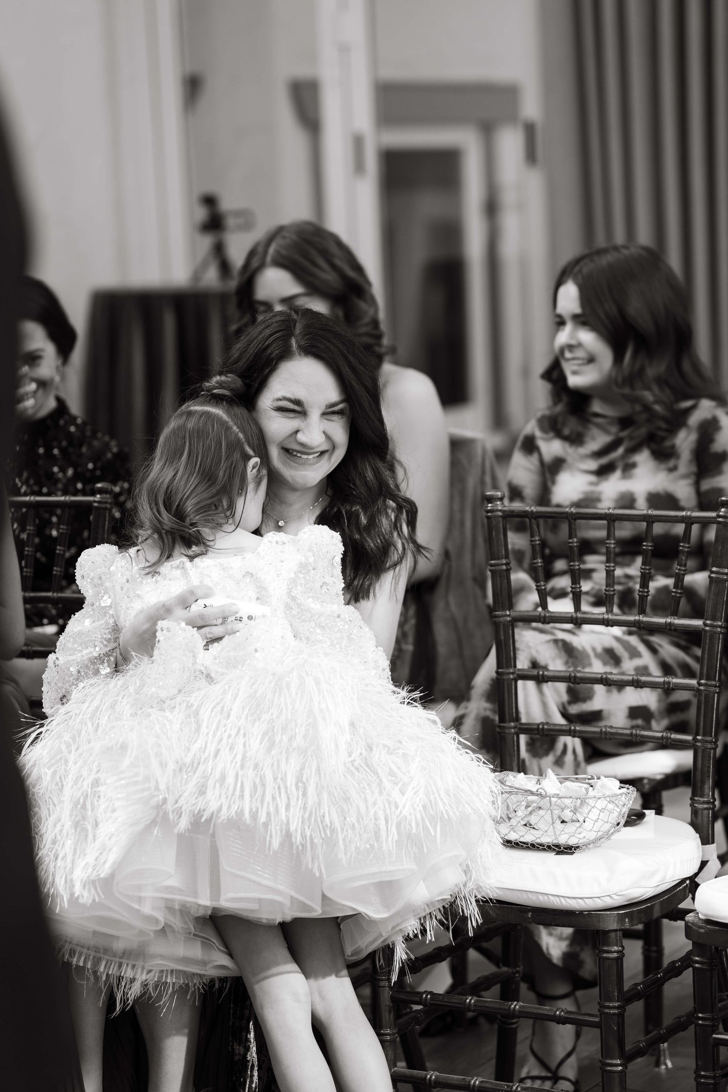 Black and white photo of a woman smiling at a young girl in a feathered white dress at an elegant event.